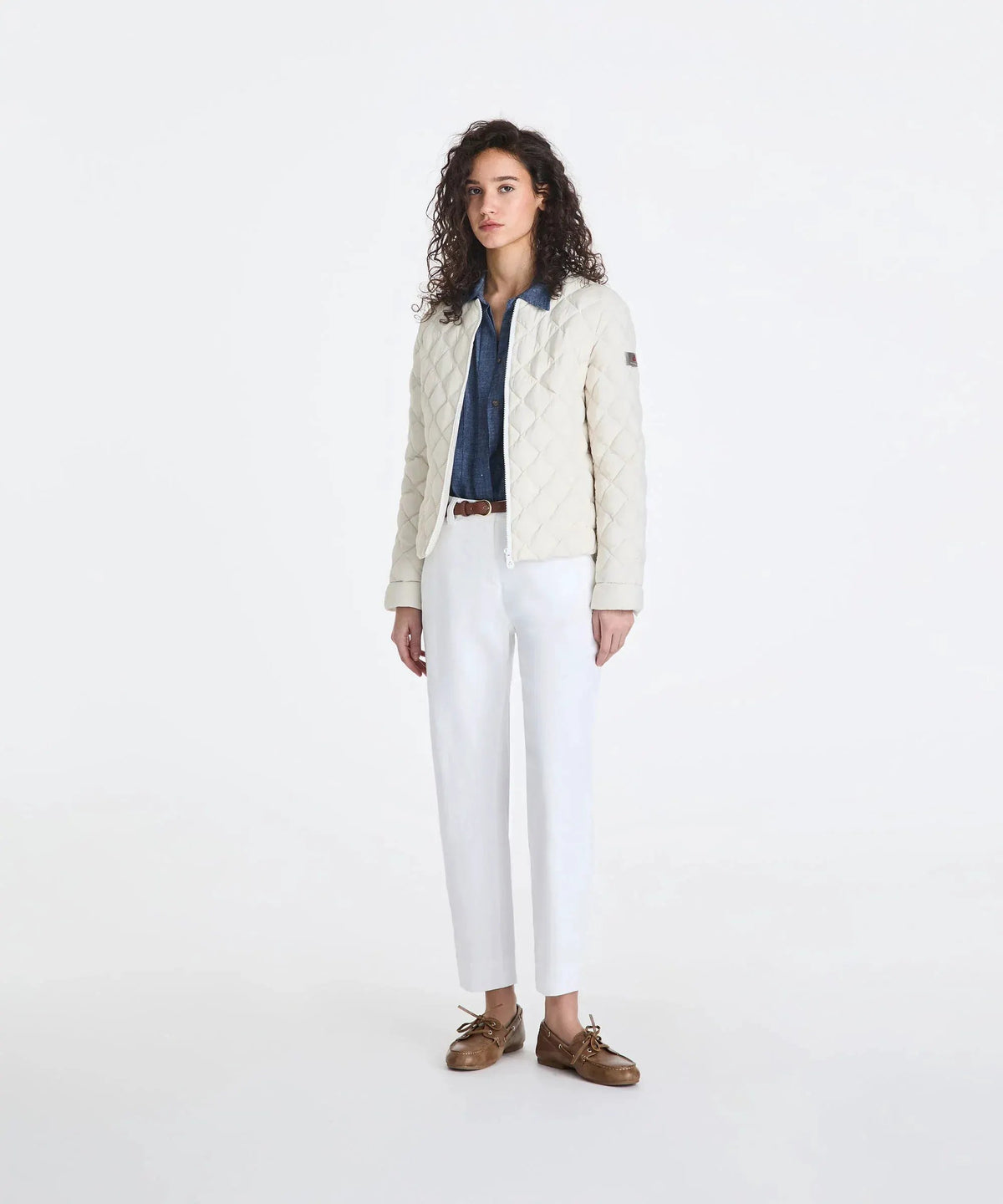 Giacca trapuntata bianca da donna, camicia denim, pantaloni bianchi e mocassini marroni