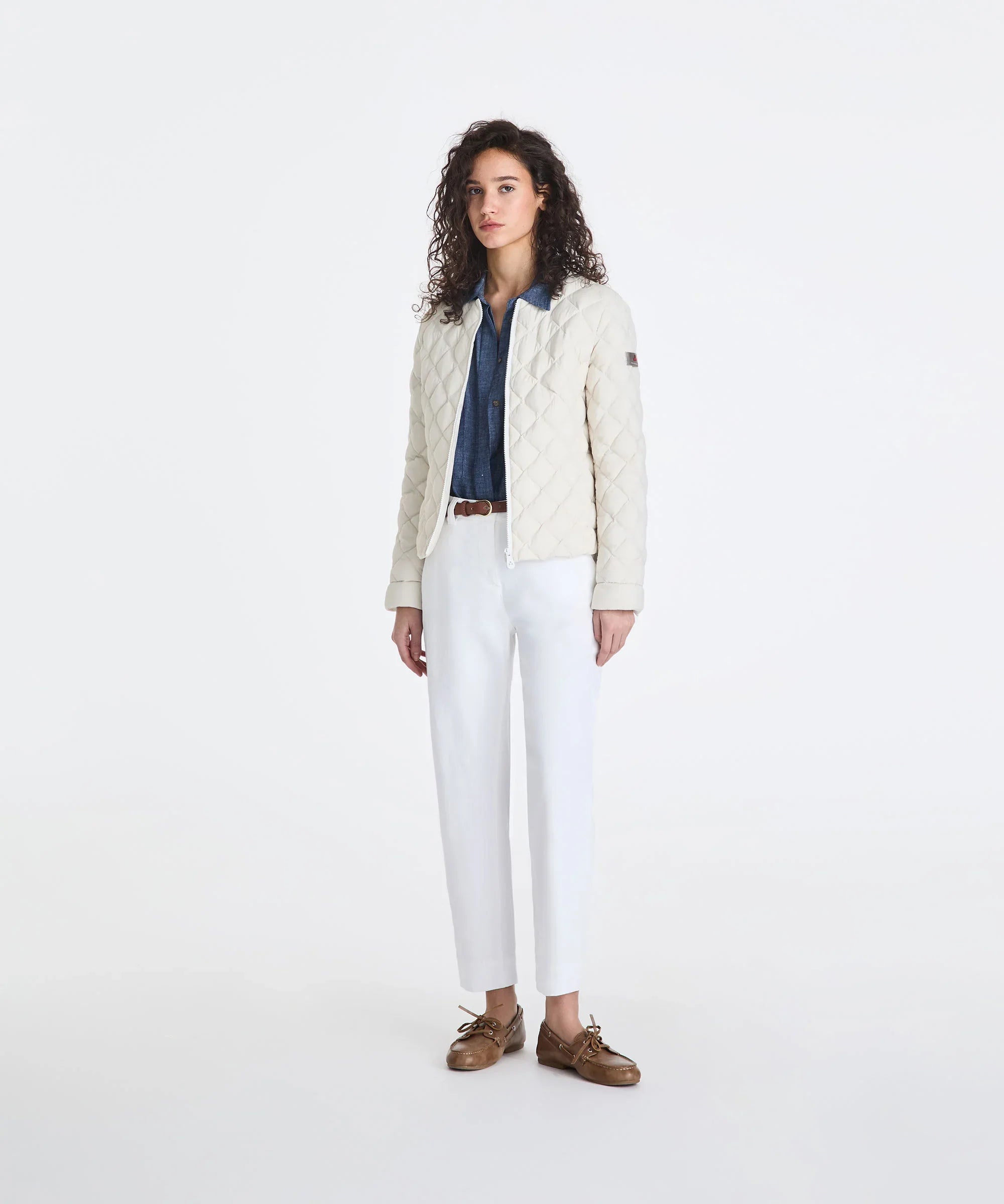 Giacca trapuntata bianca da donna, camicia denim, pantaloni bianchi e mocassini marroni