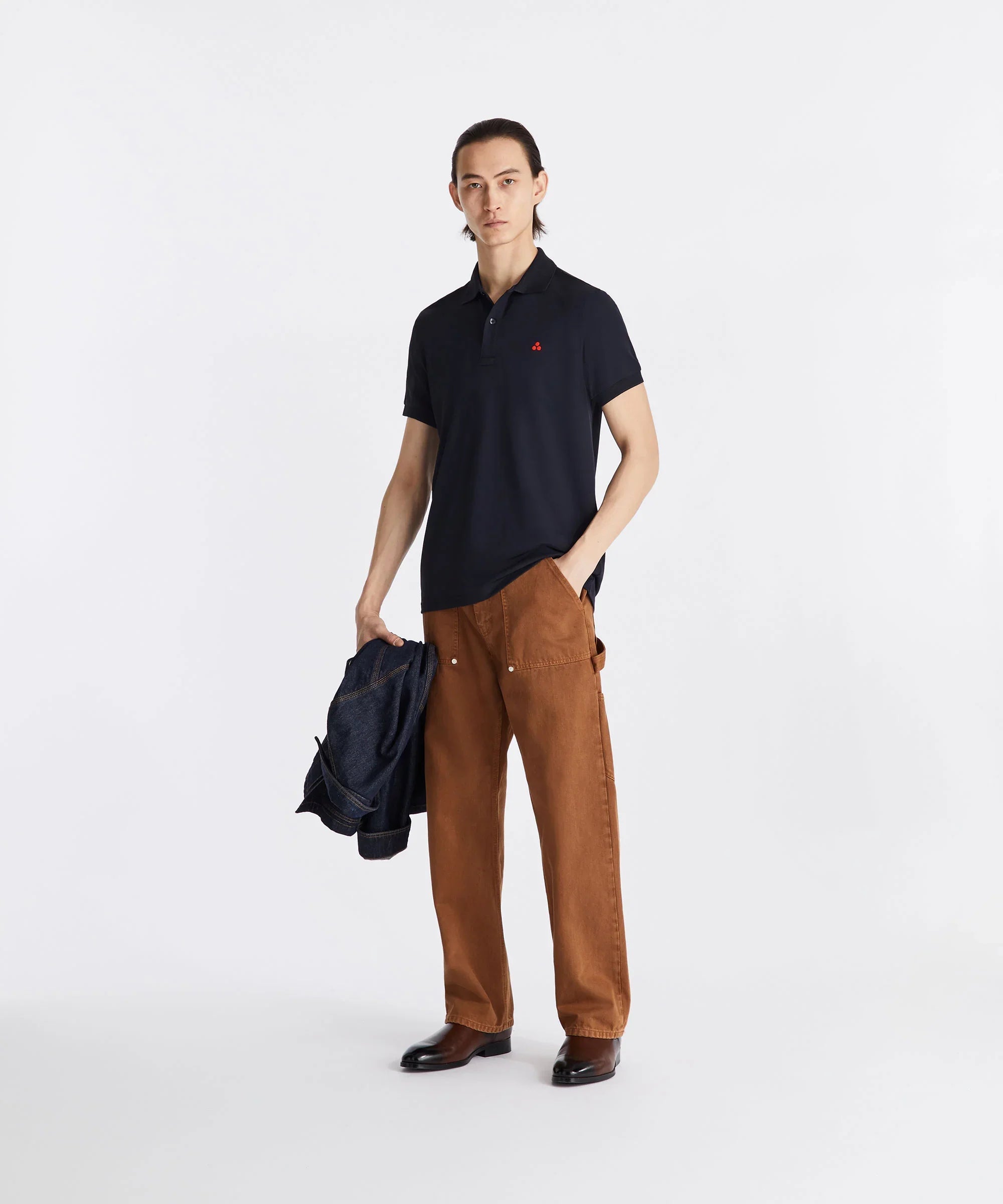 Modello uomo con polo nera, pantaloni marroni larghi e giacca in denim, look casual elegante.