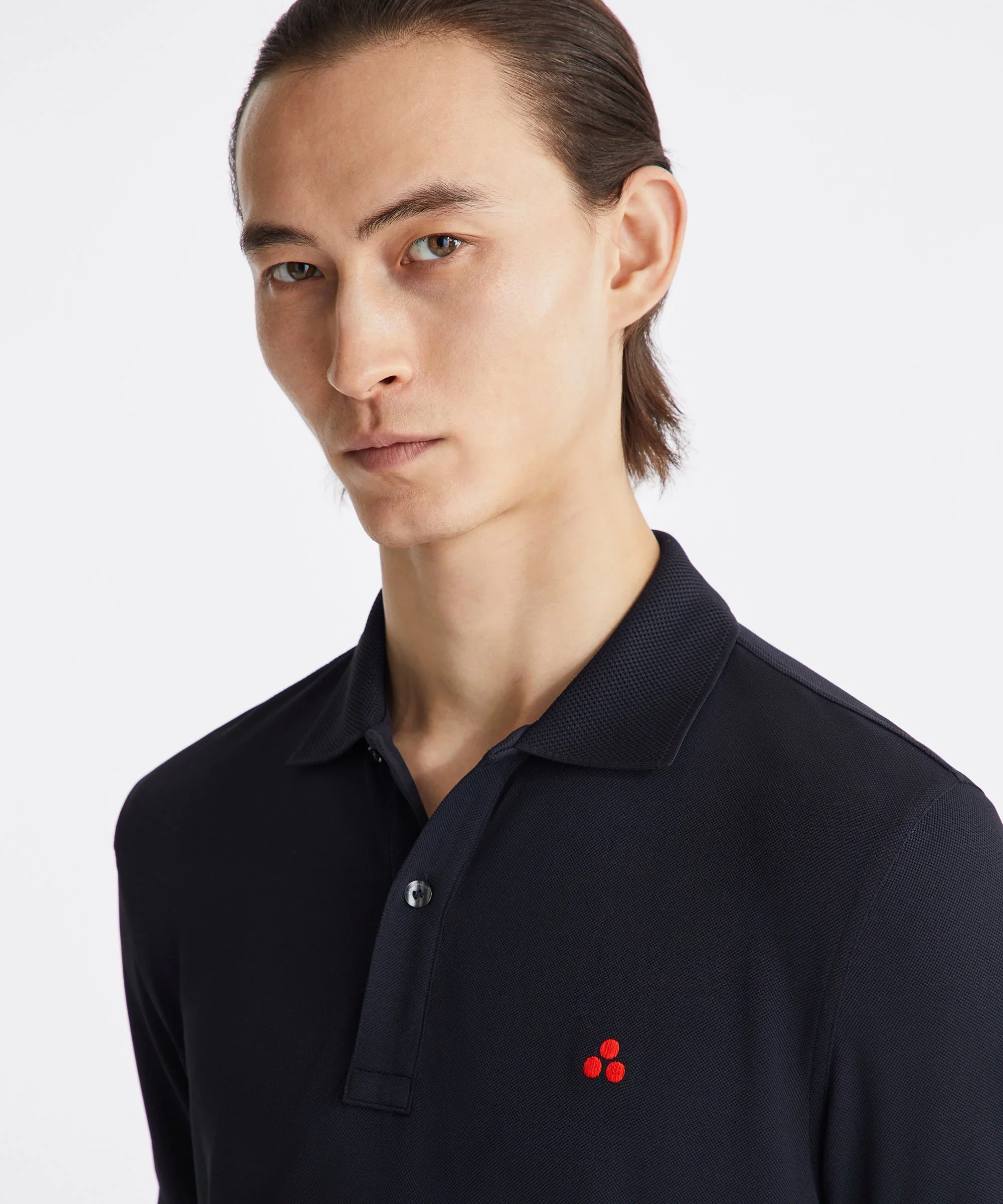 Uomo indossa polo nera Peuterey con logo rosso ricamato, sfondo bianco minimal.