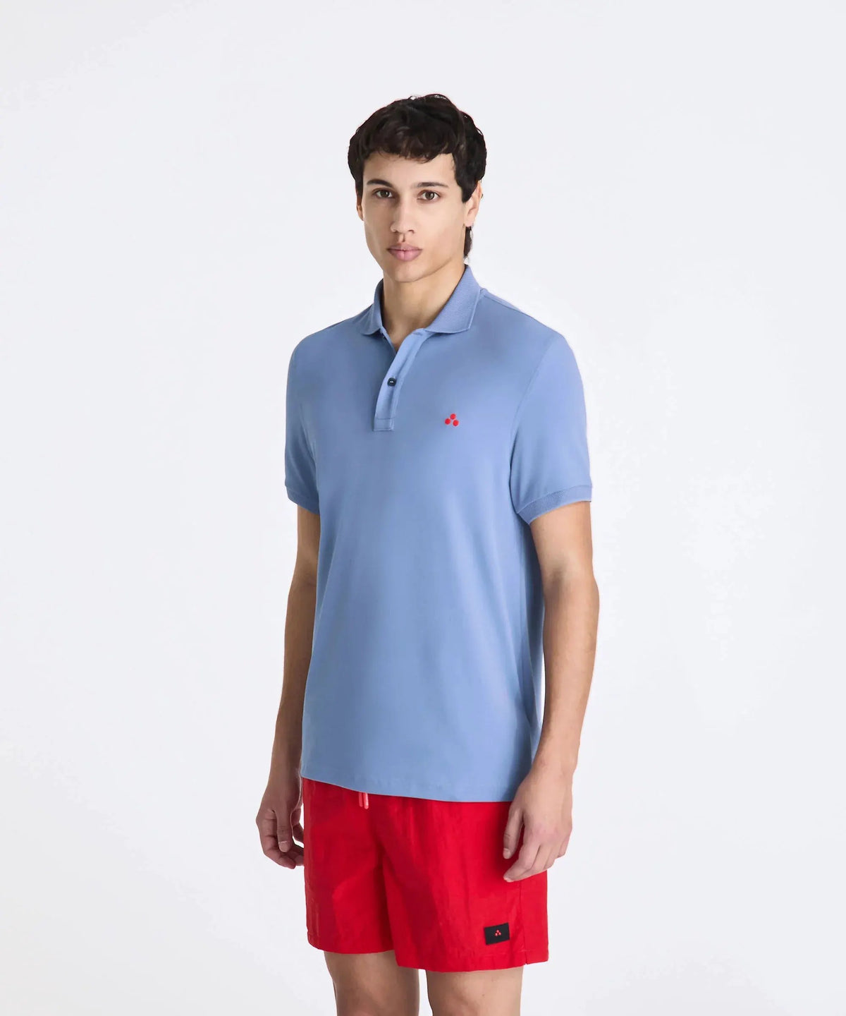 Modello indossa polo azzurra con logo rosso e pantaloncini rossi, moda uomo estiva.