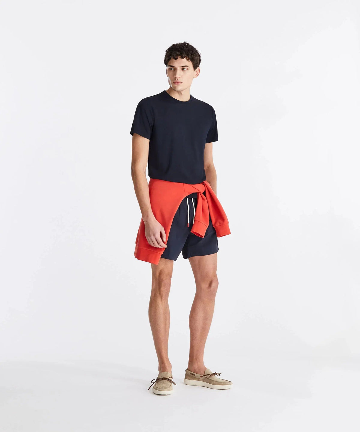 Modello con t-shirt blu, pantaloncini navy, felpa arancione e mocassini beige, moda uomo casual