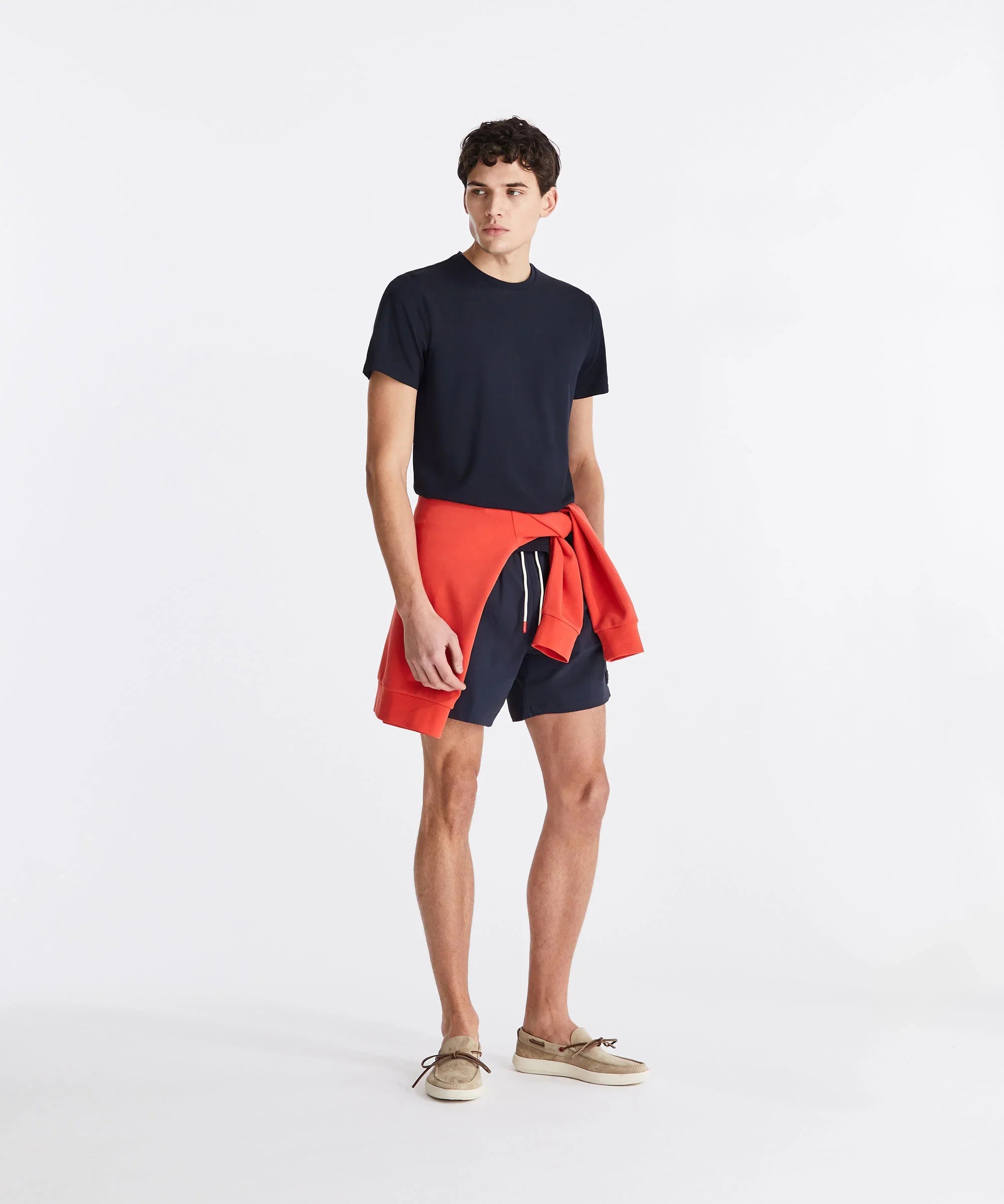 Modello con t-shirt blu, pantaloncini navy, felpa arancione e mocassini beige, moda uomo casual