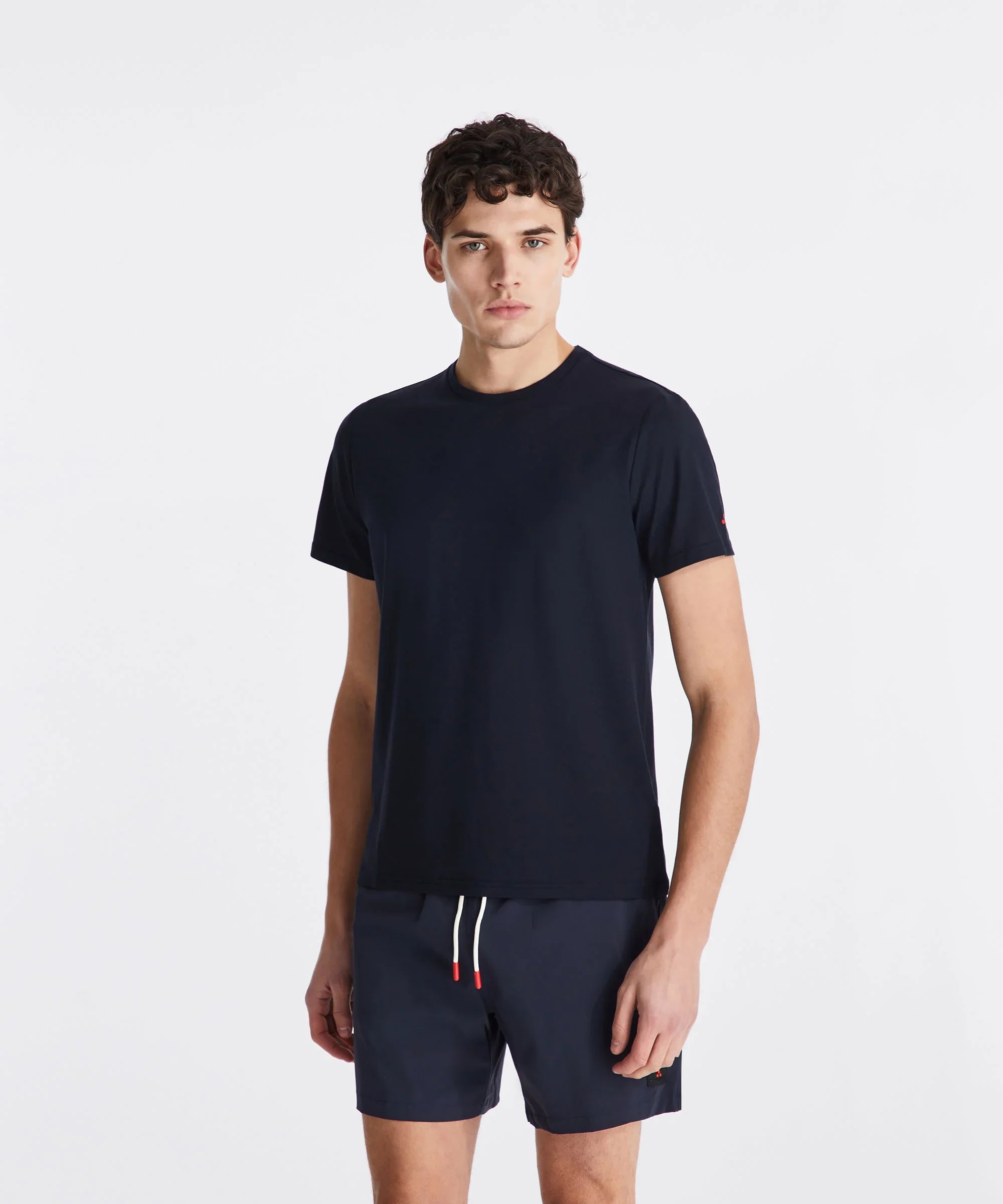 Modello uomo indossa t-shirt blu navy e pantaloncini corti in tessuto tecnico, sfondo bianco