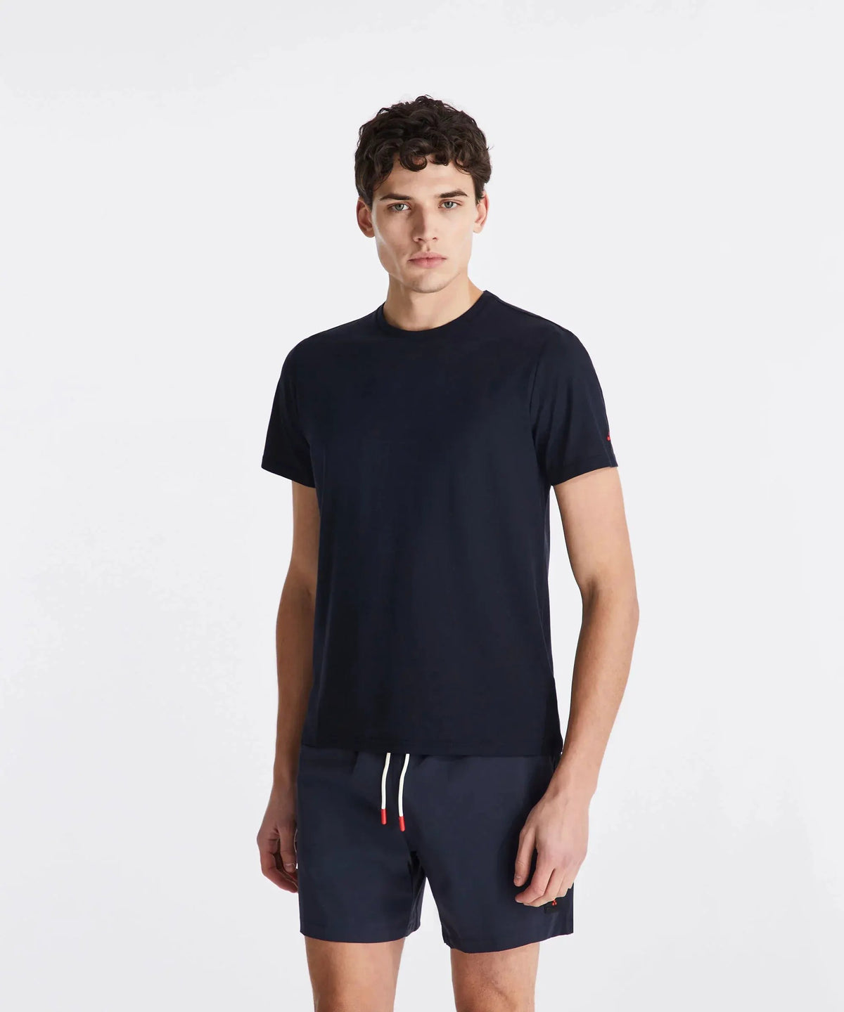 Modello uomo indossa t-shirt blu navy e pantaloncini corti in tessuto tecnico, sfondo bianco