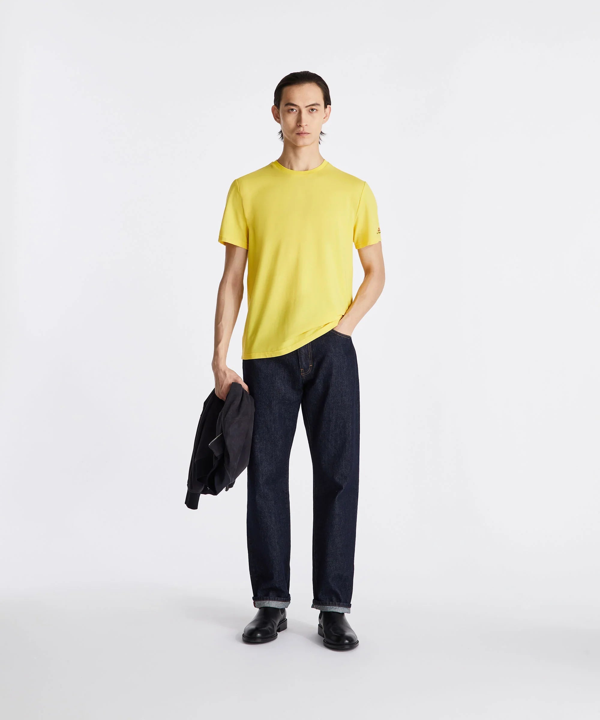 Uomo con t-shirt gialla e jeans blu scuro, look casual moderno su sfondo bianco