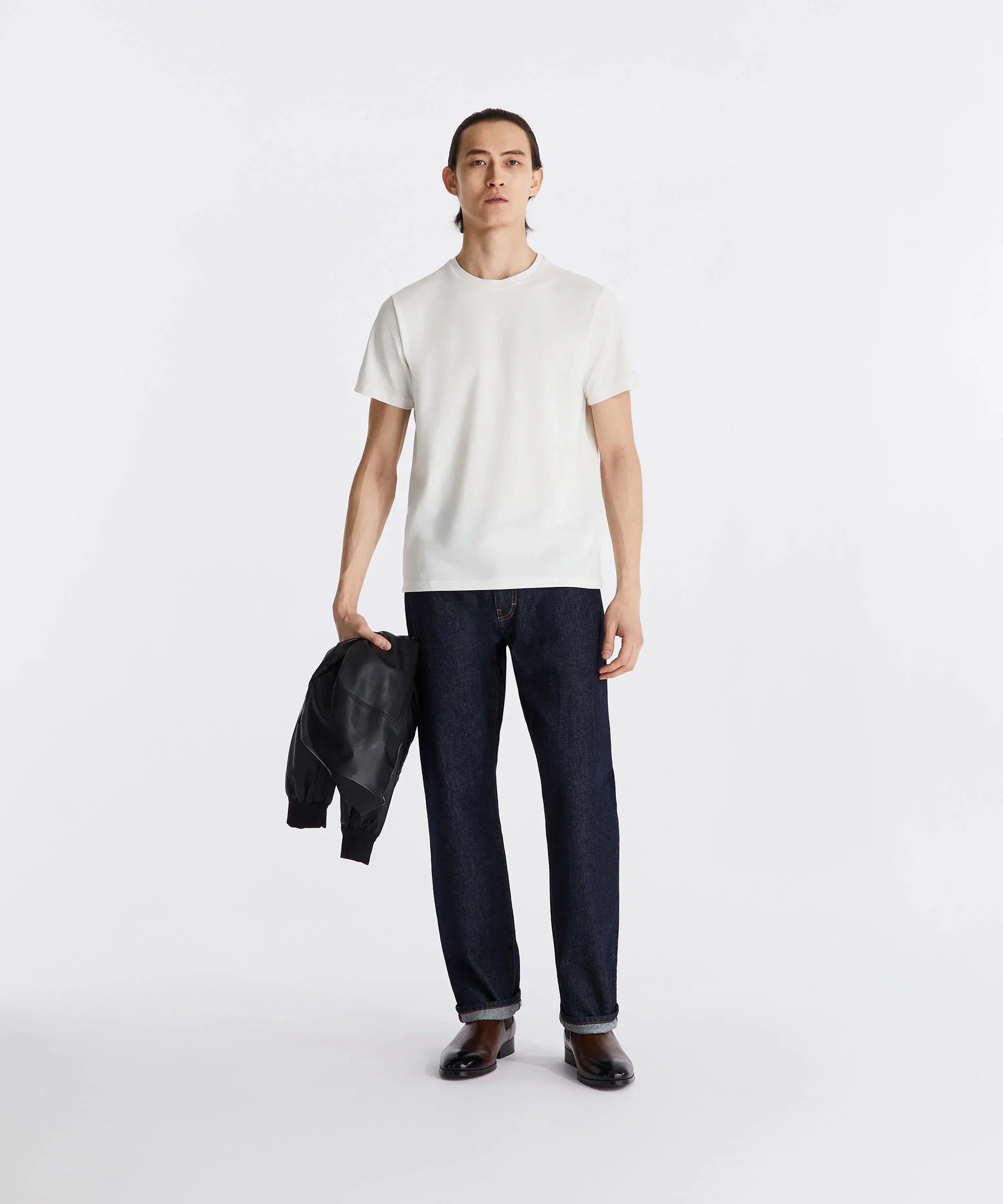 Modello uomo con t-shirt bianca, jeans blu dritti e giacca nera in mano, look casual moda uomo