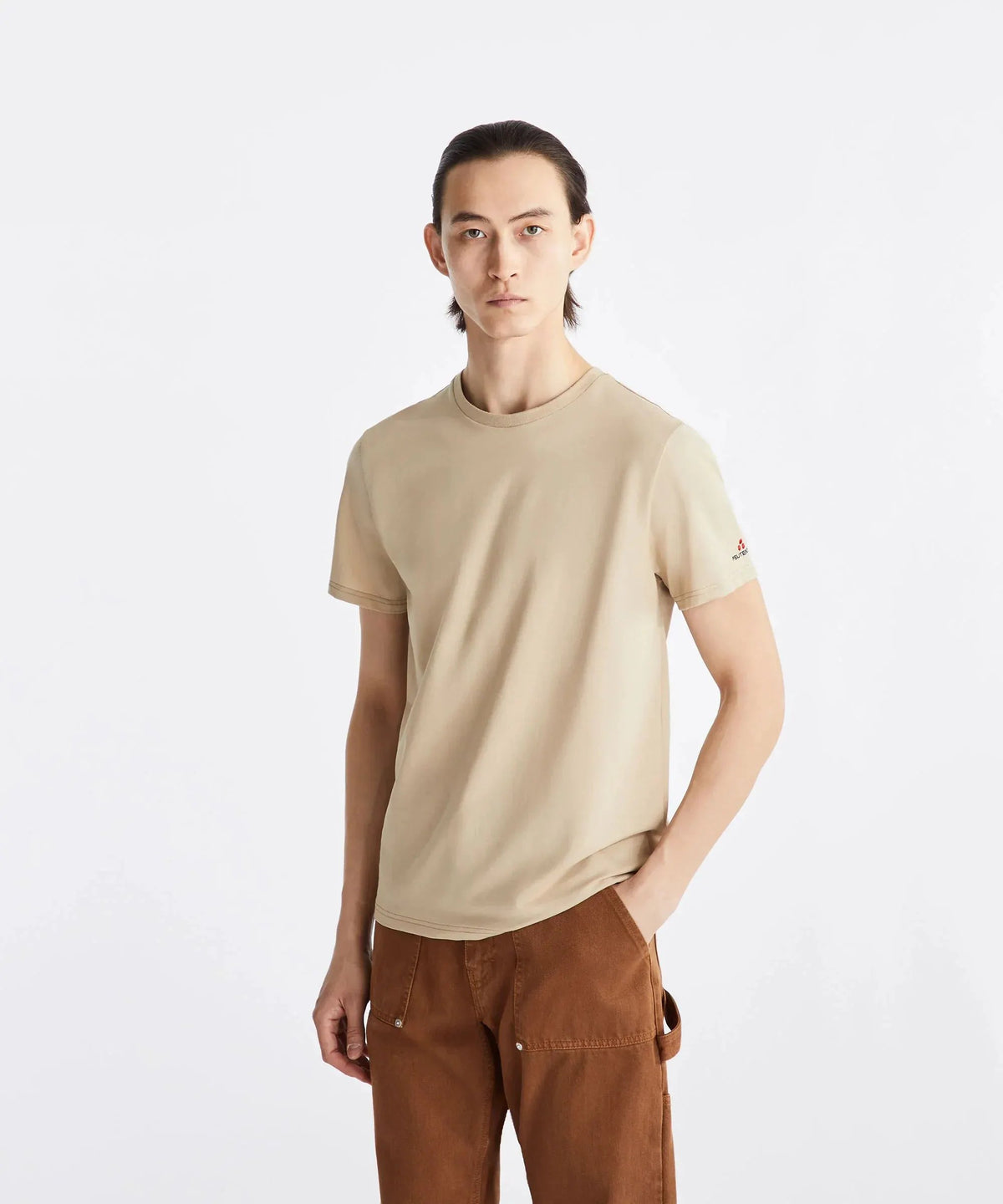 Modello uomo con t-shirt beige Peuterey e pantaloni marroni, sfondo bianco, moda casual