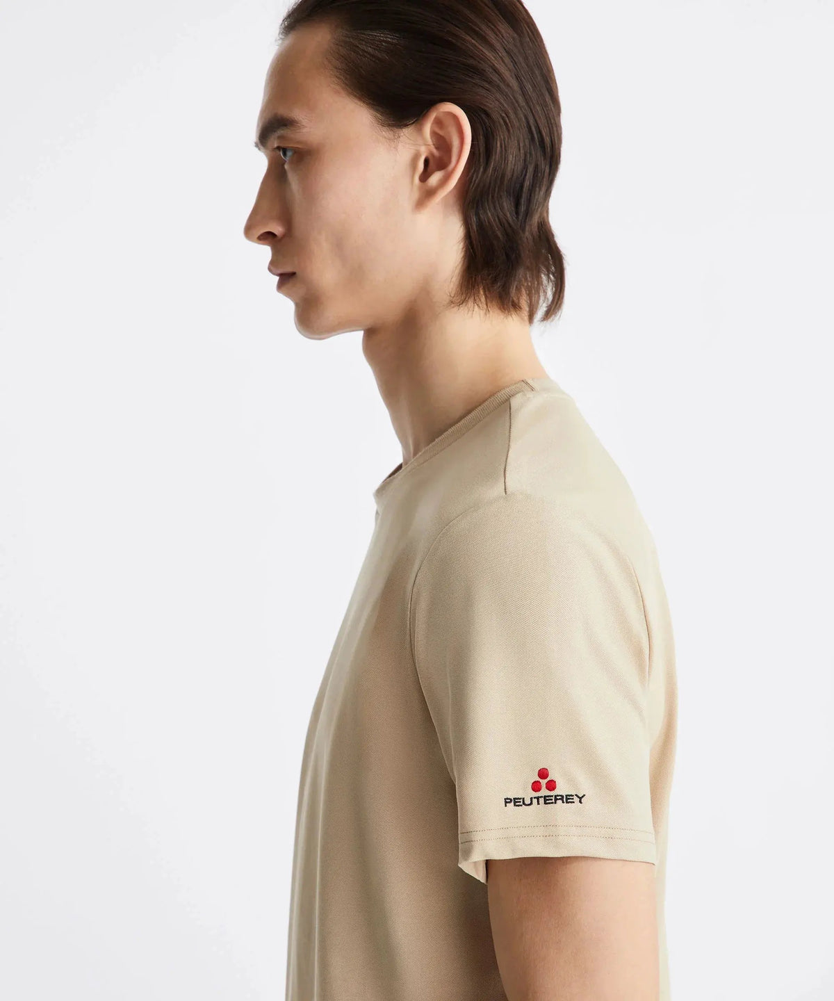 Uomo di profilo con t-shirt beige Peuterey, logo ricamato su manica, sfondo bianco