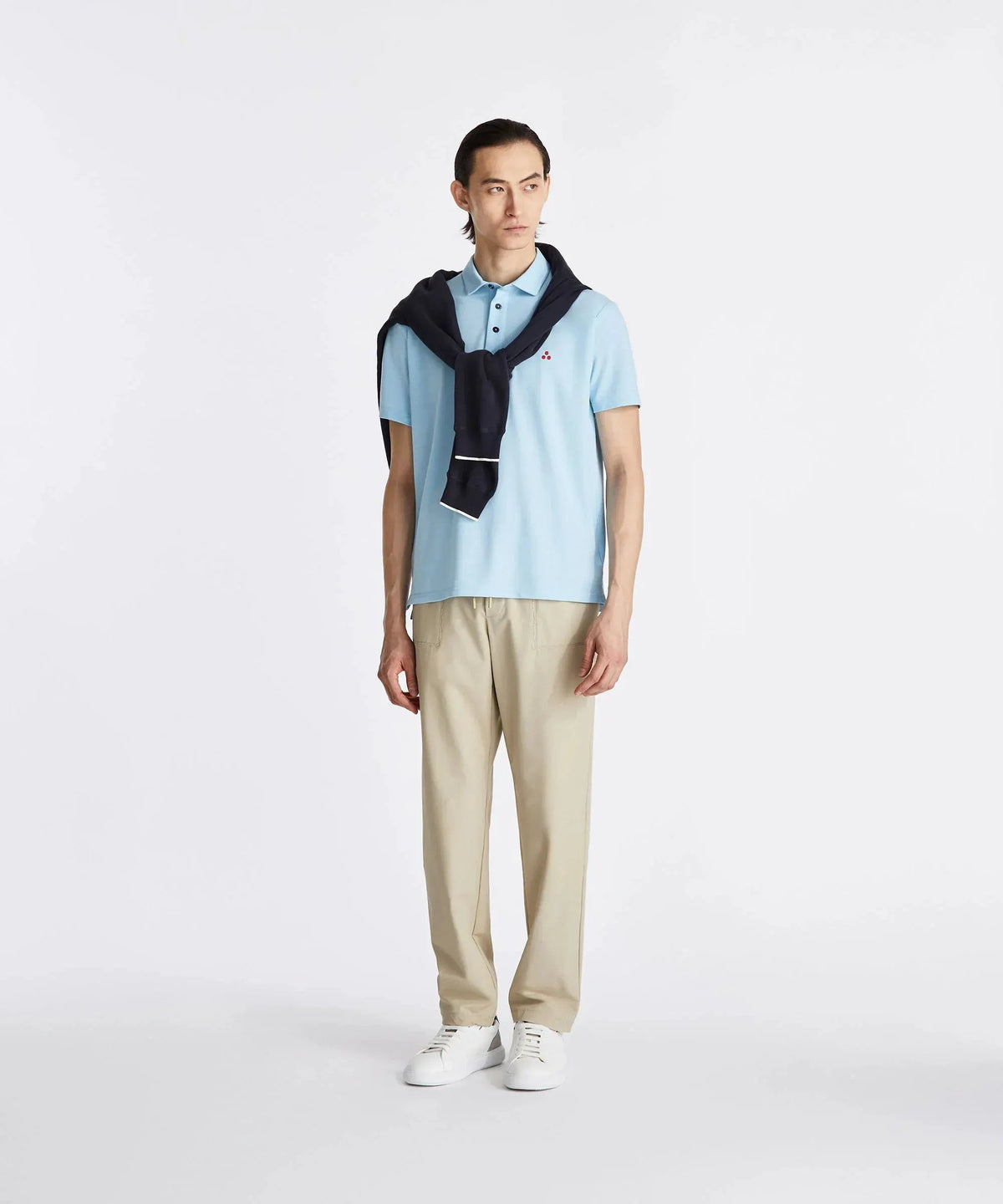 Modello uomo con polo celeste, pantaloni beige, sneakers bianche e maglia blu sulle spalle