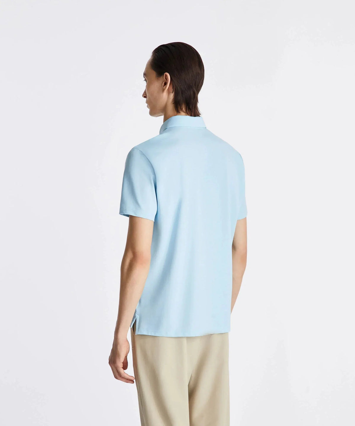Uomo di spalle con polo azzurra a maniche corte e pantaloni beige eleganti