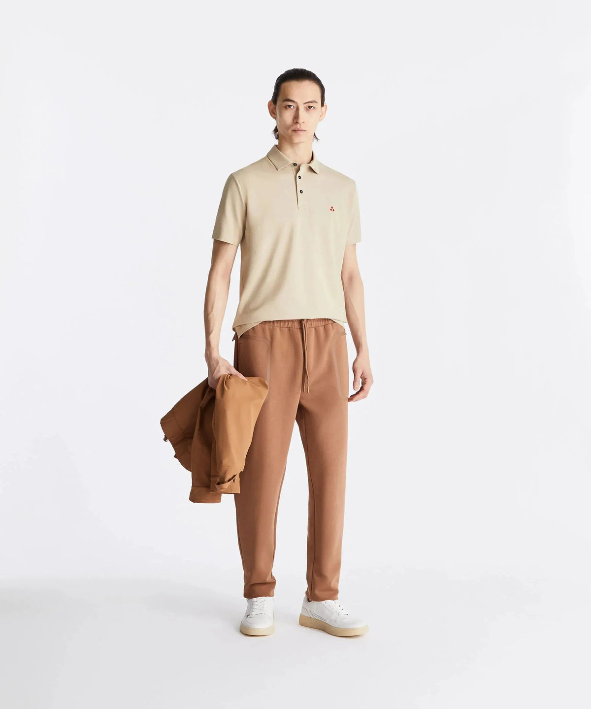 Modello con polo beige, pantaloni marroni e sneakers bianche, moda uomo casual elegante.