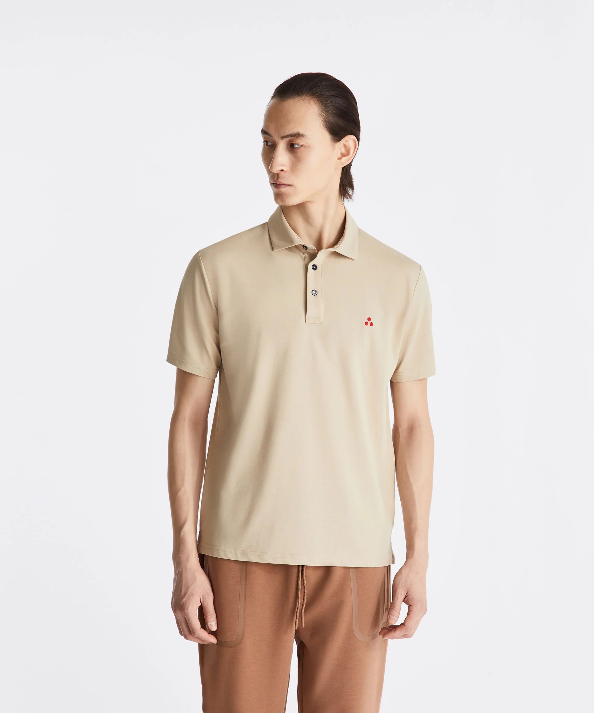 Uomo con polo beige a maniche corte e pantaloni marroni, sfondo bianco minimalista