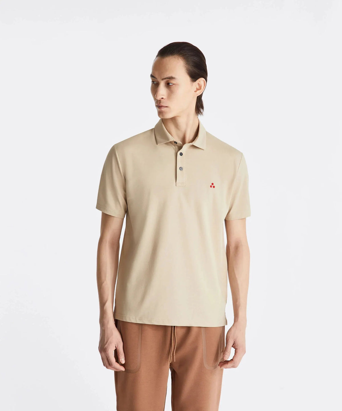 Uomo con polo beige a maniche corte e pantaloni marroni, sfondo bianco minimalista