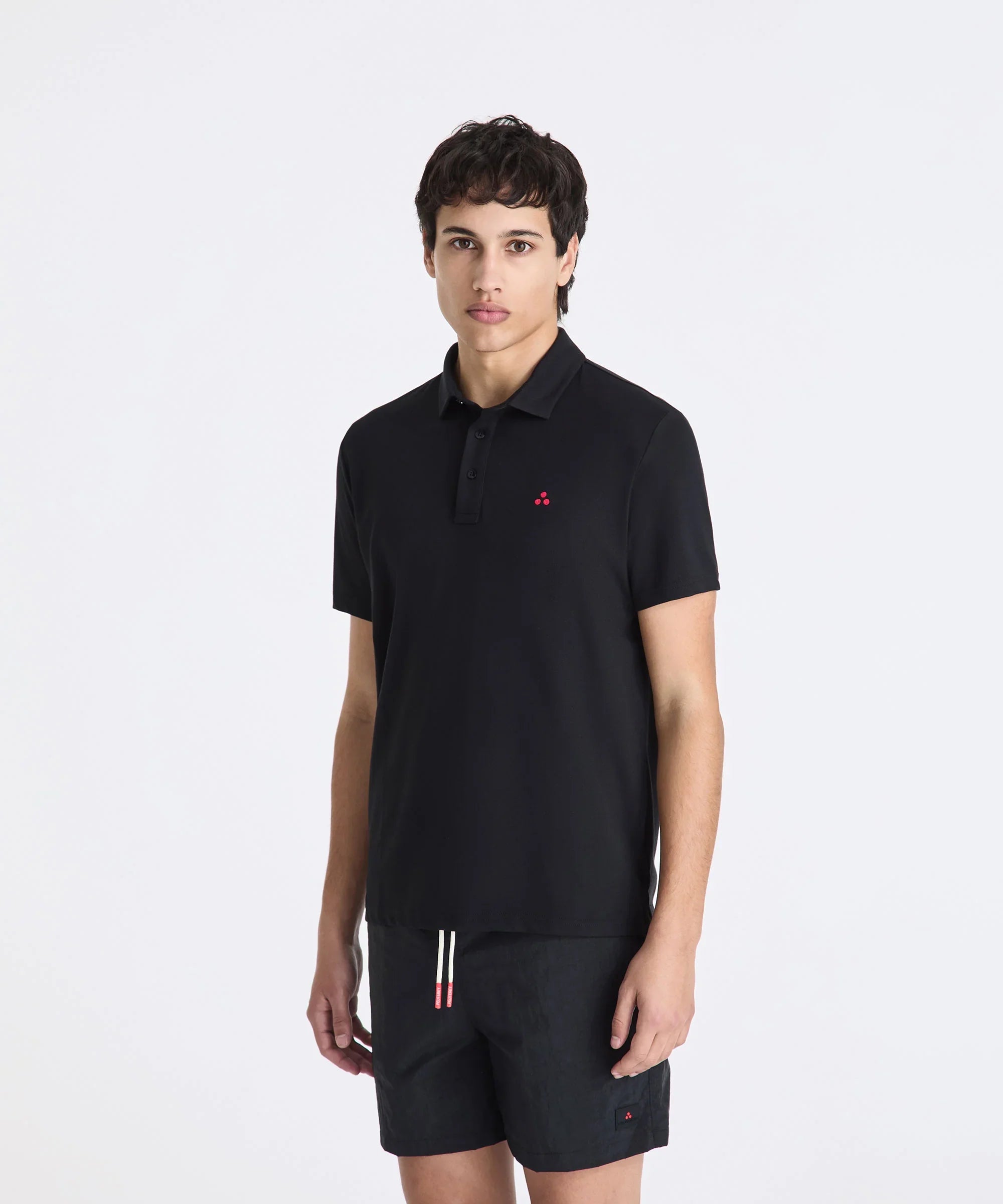 Modello indossa polo nera Peuterey classica e bermuda neri su sfondo bianco