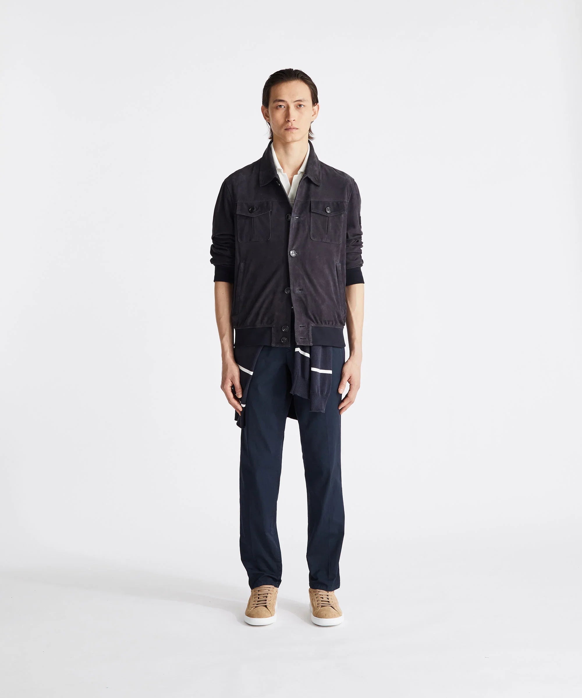 Modello indossa giacca blu scuro, pantaloni blu e sneakers beige su sfondo bianco.