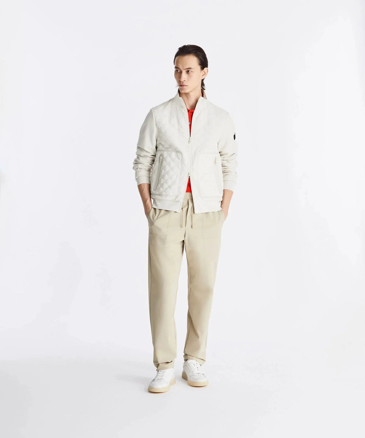 Modello uomo con giacca trapuntata bianca, pantaloni beige e sneakers bianche, su sfondo neutro