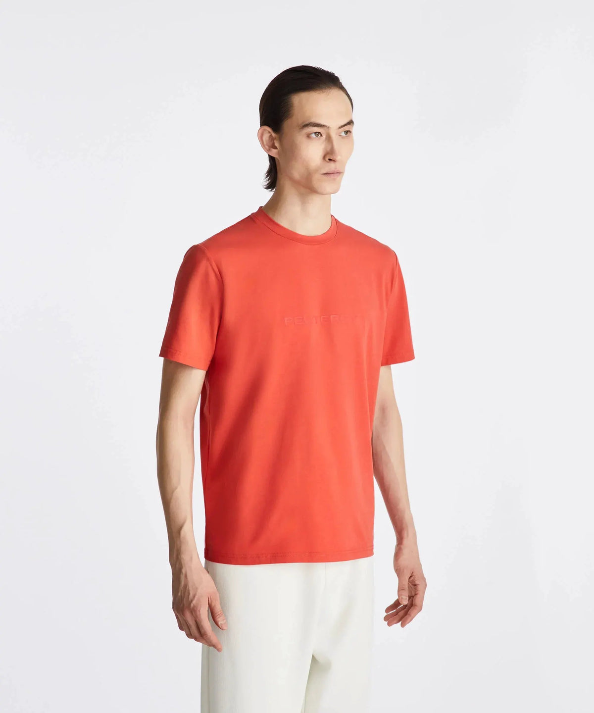 Modello con t-shirt Peuterey arancione da uomo e pantaloni bianchi su sfondo bianco