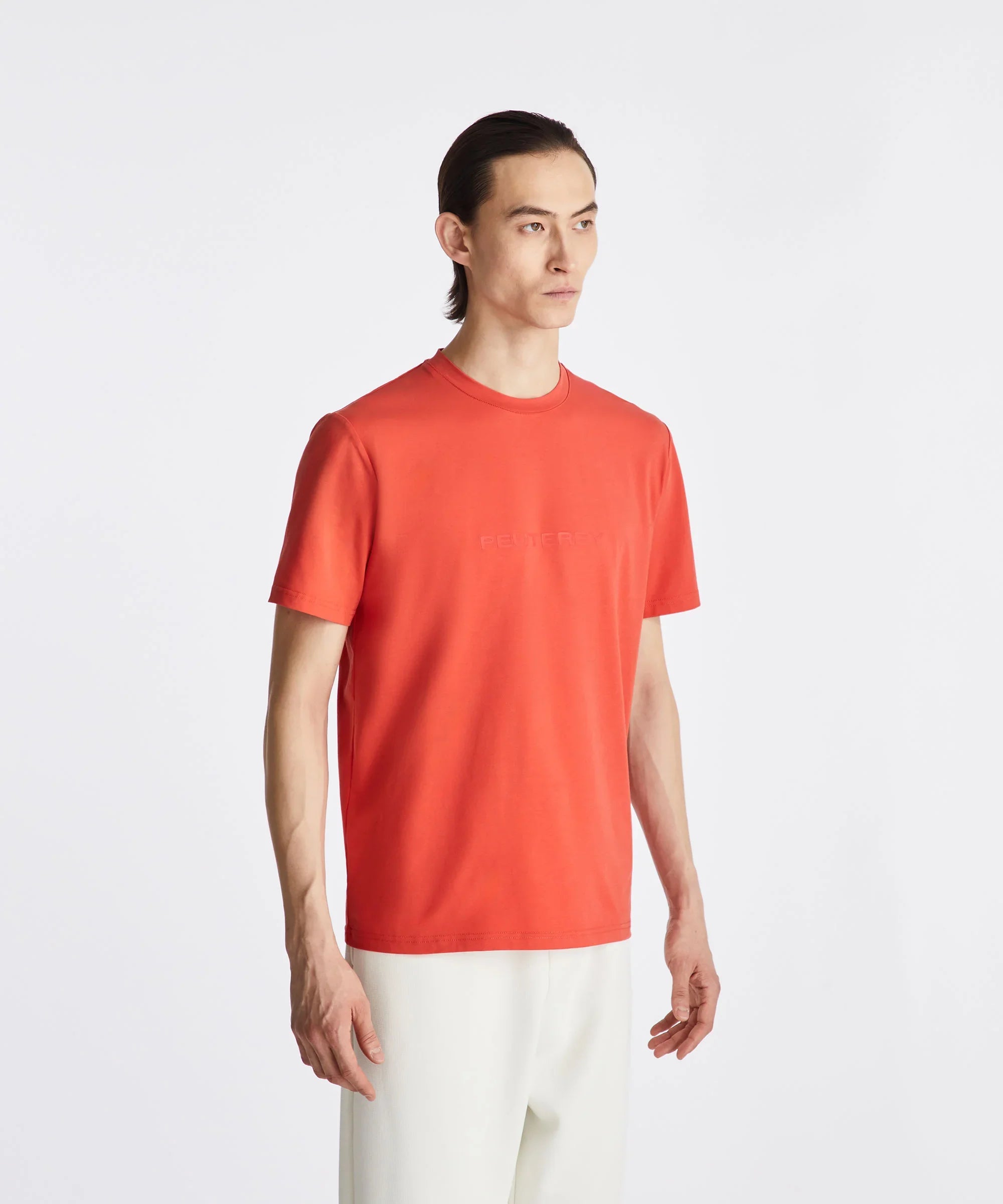 Modello con t-shirt Peuterey arancione da uomo e pantaloni bianchi su sfondo bianco