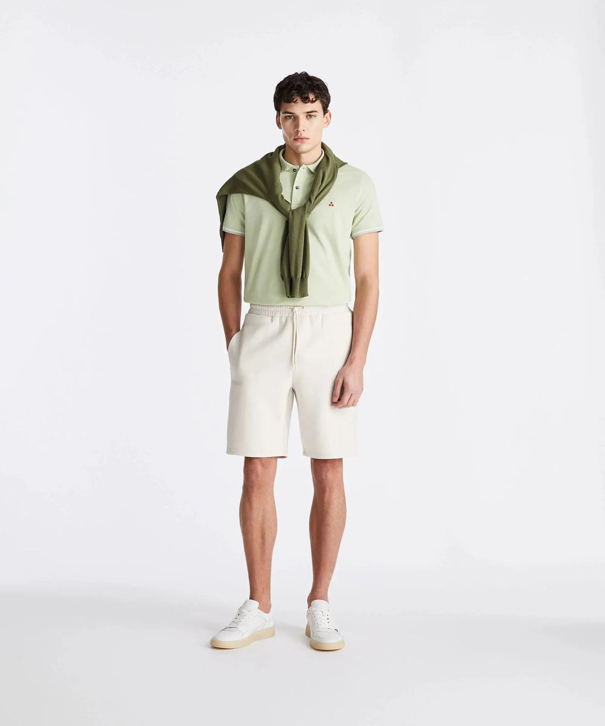 Modello uomo indossa polo verde chiaro, bermuda beige e sneakers bianche, stile casual elegante.