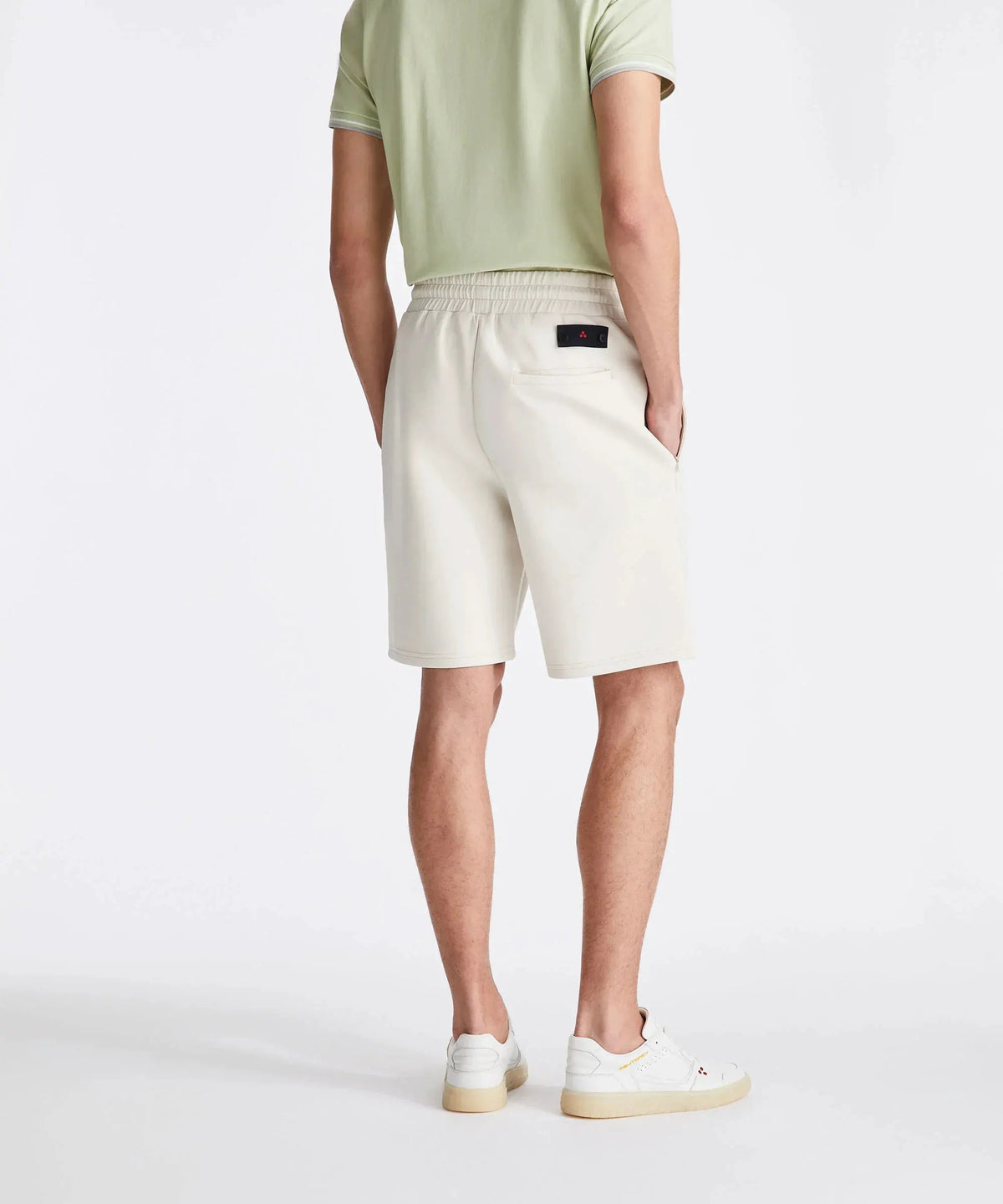 Bermuda uomo panna in tessuto tecnico con elastico, indossato con polo verde chiaro e sneakers bianche.