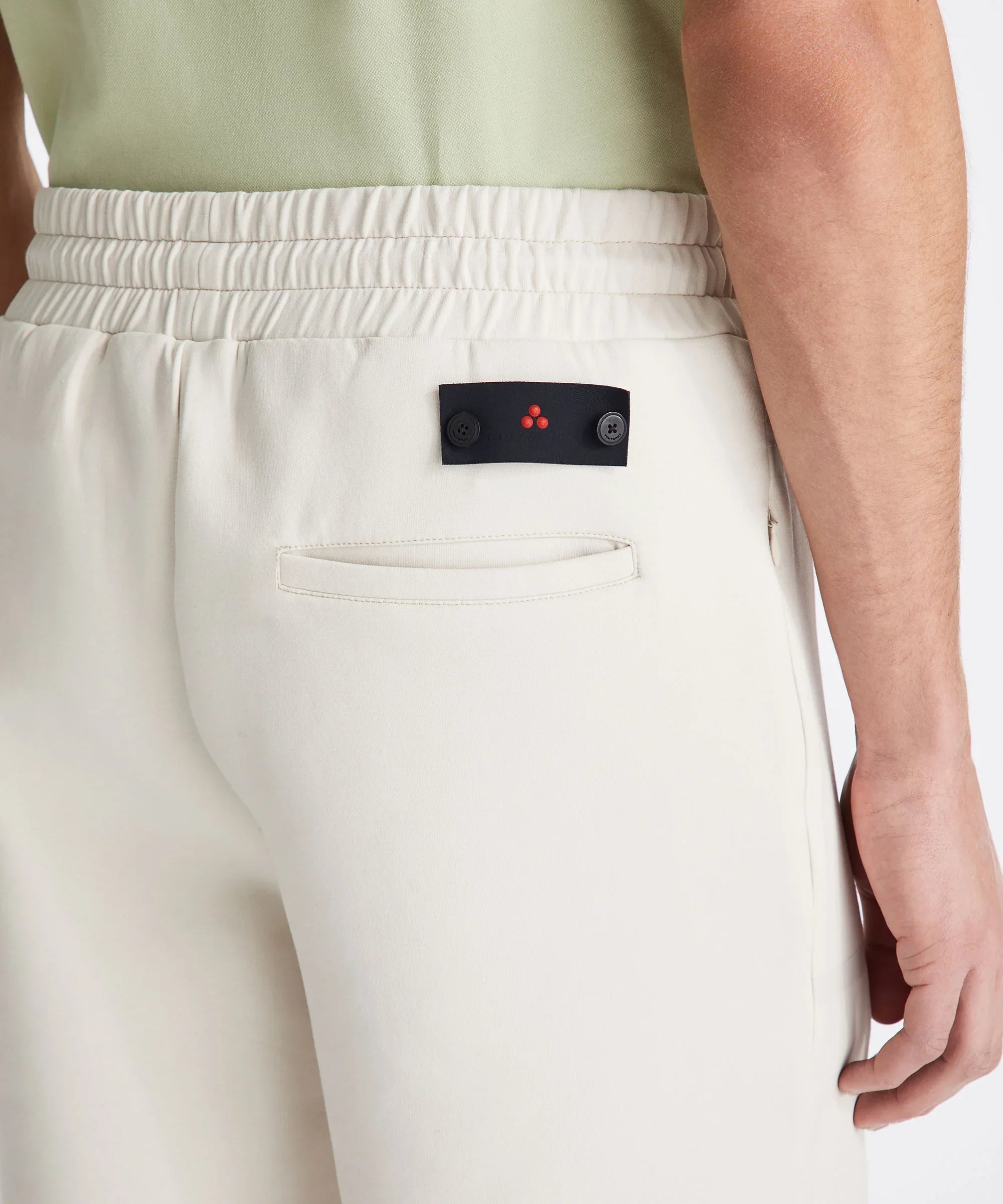 Dettaglio pantaloni uomo beige elasticizzati con tasca posteriore e logo minimal