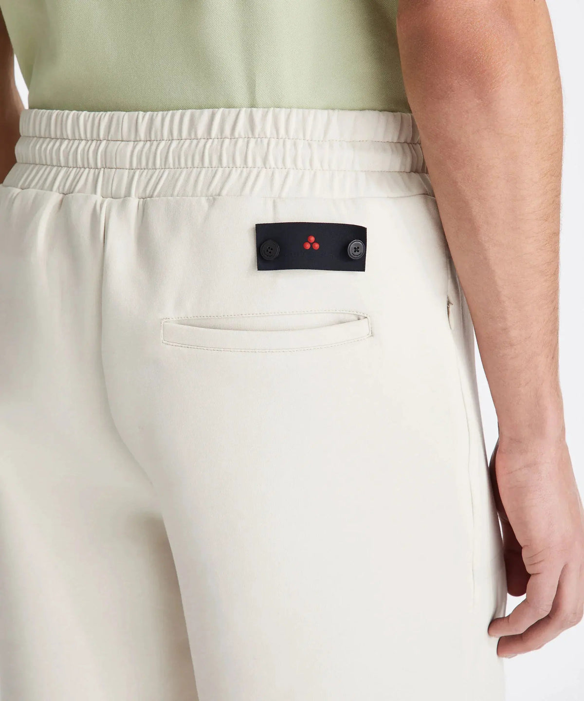 Dettaglio pantaloni uomo beige elasticizzati con tasca posteriore e logo minimal