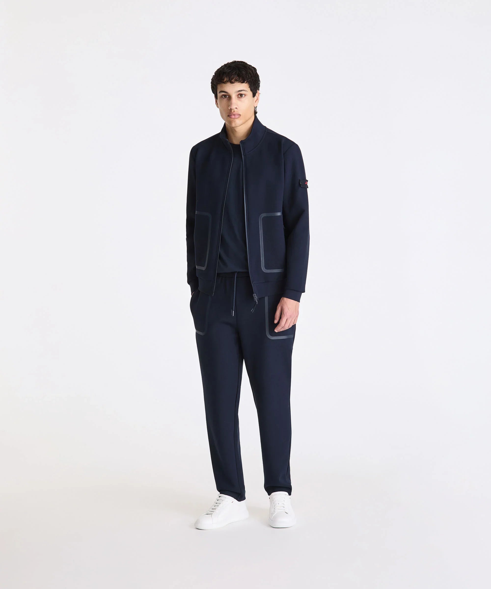 Completo uomo tuta blu navy con giacca zip, pantaloni sportivi e sneakers bianche.