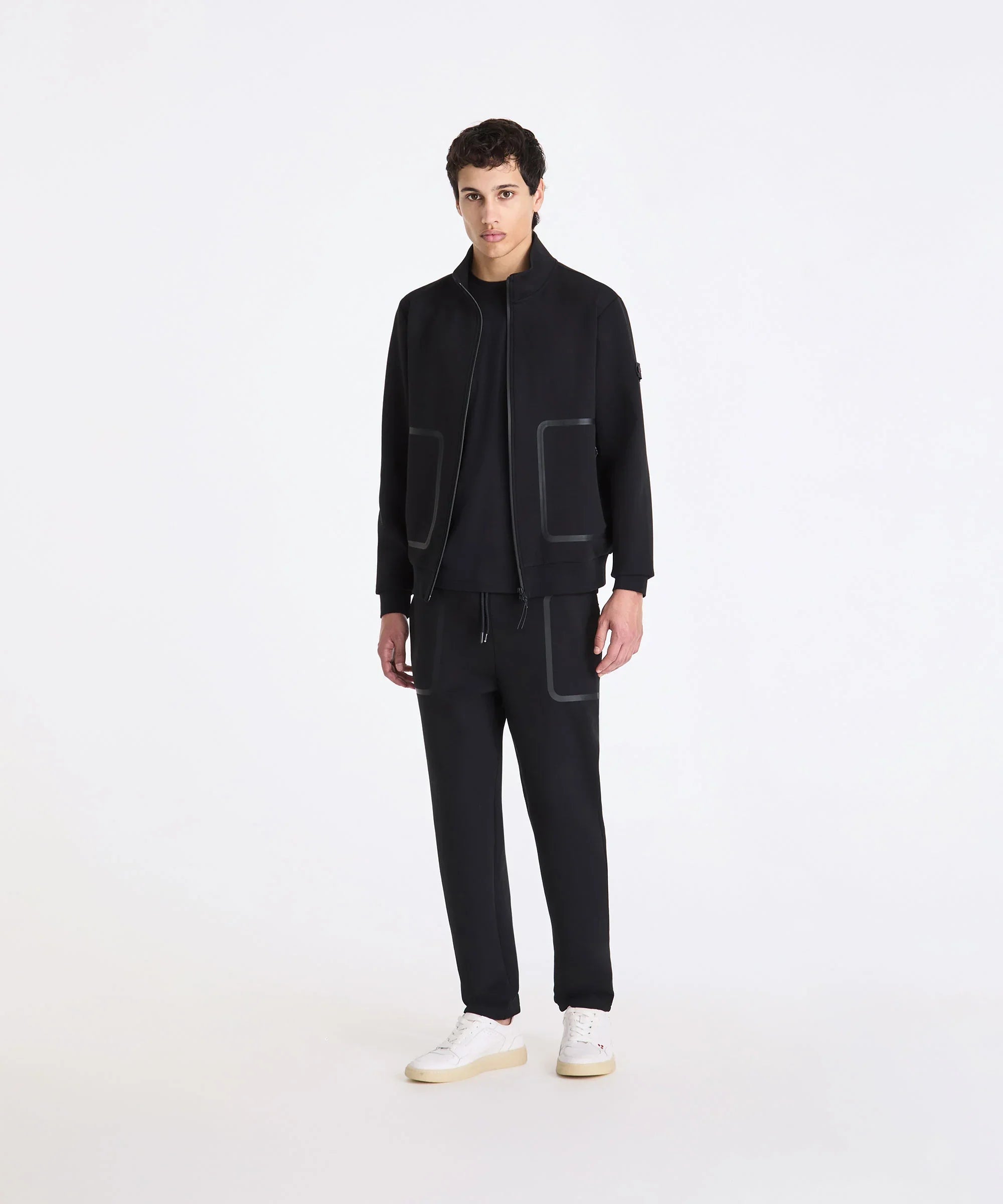 Completo tuta uomo nero con zip, tasche grandi e sneakers bianche, moda casual elegante