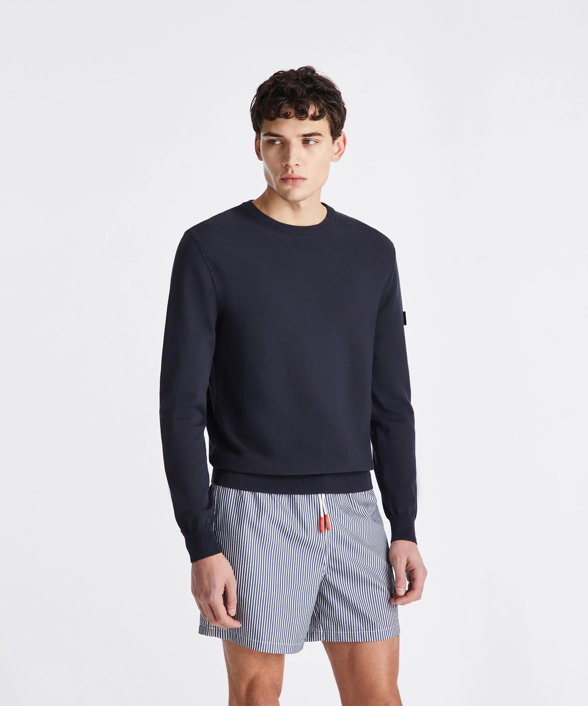 Modello uomo con maglia blu a maniche lunghe e shorts rigati bianchi e blu, sfondo neutro.