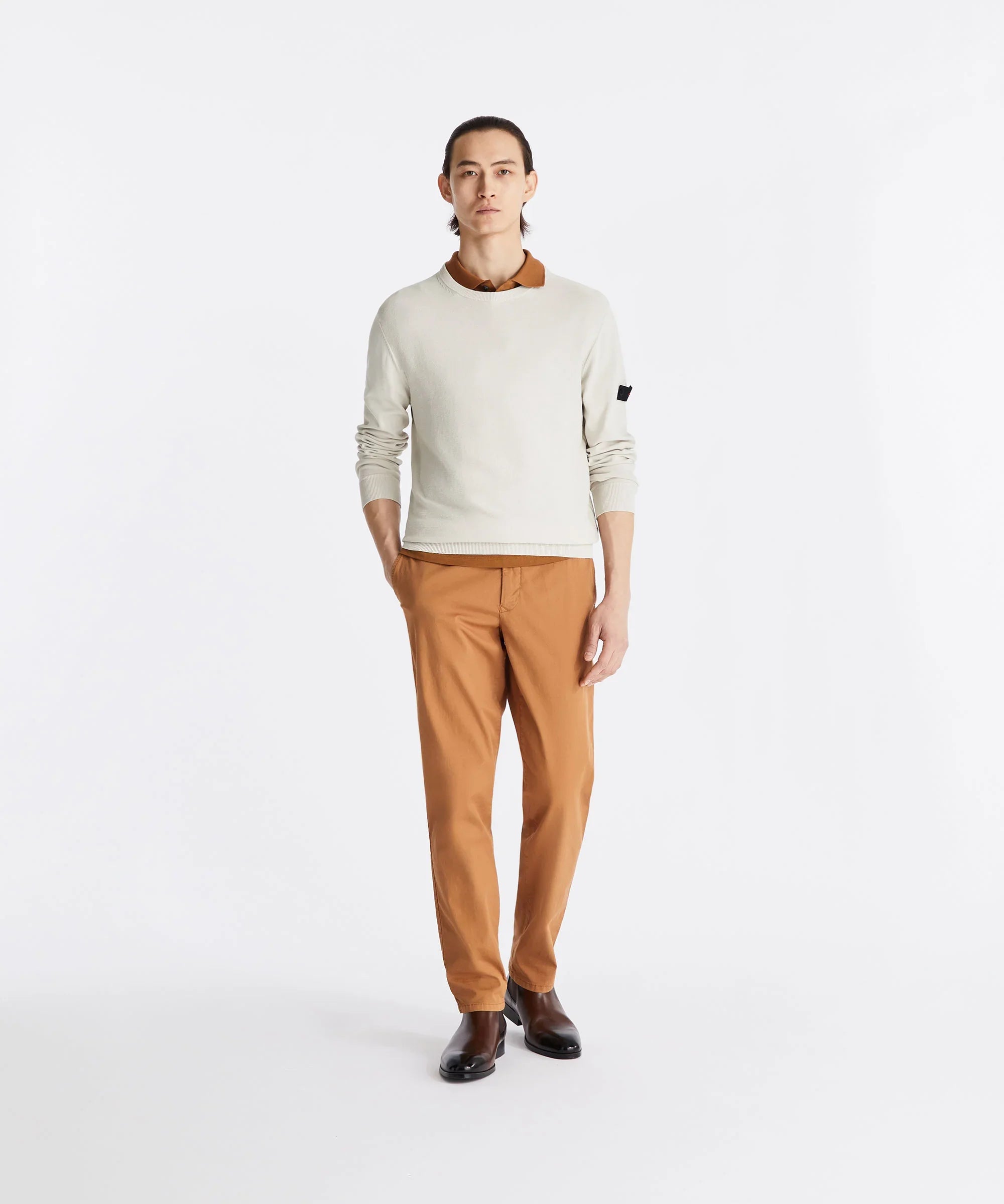Modello uomo indossa maglione beige, pantaloni color caramello e stivali neri eleganti