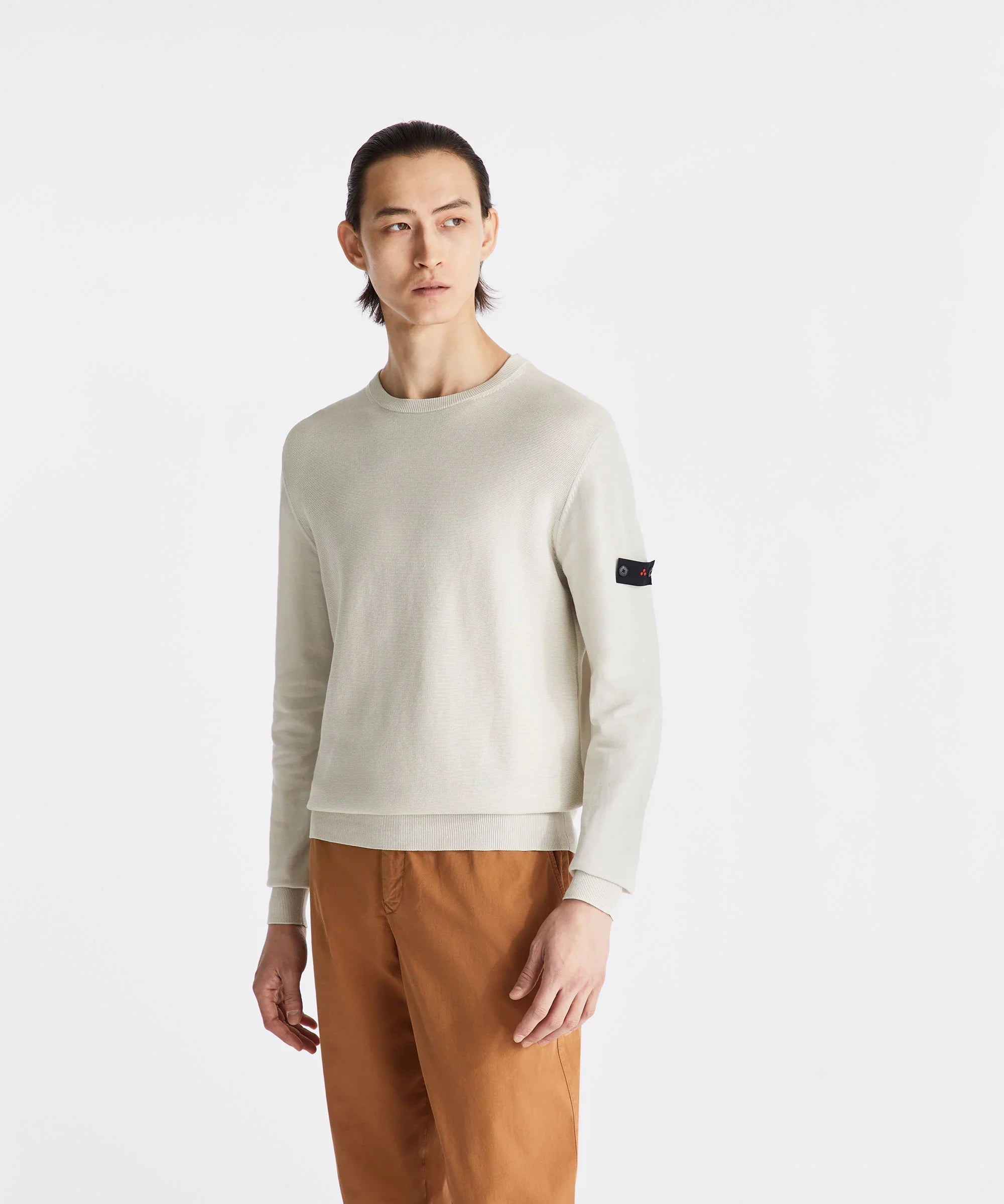 Modello indossa maglia uomo beige a maniche lunghe con toppa nera su manica e pantaloni marroni.