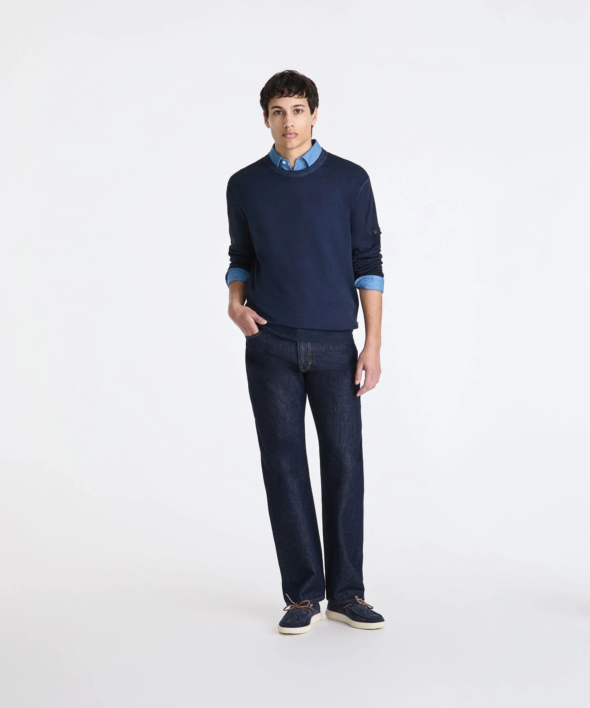 Modello uomo indossa maglione blu, camicia denim, jeans scuri e mocassini, moda casual.