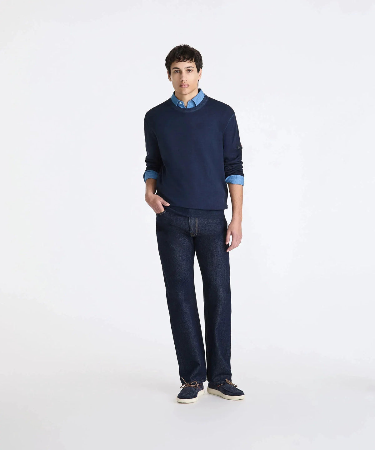 Modello uomo indossa maglione blu, camicia denim, jeans scuri e mocassini, moda casual.