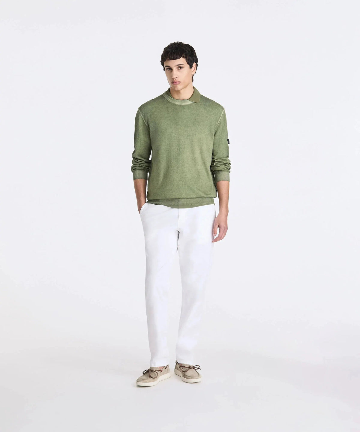 Modello uomo con maglione verde, pantaloni bianchi e mocassini beige su sfondo neutro