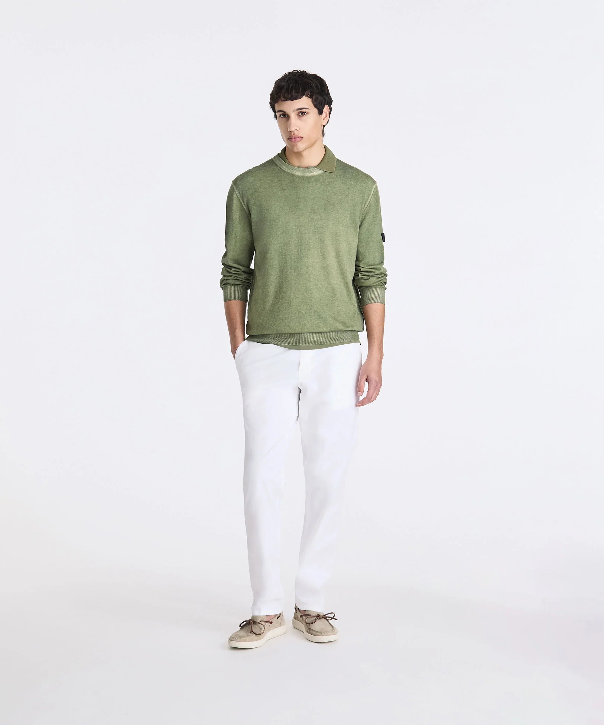 Modello uomo con maglione verde, pantaloni bianchi e mocassini beige su sfondo neutro