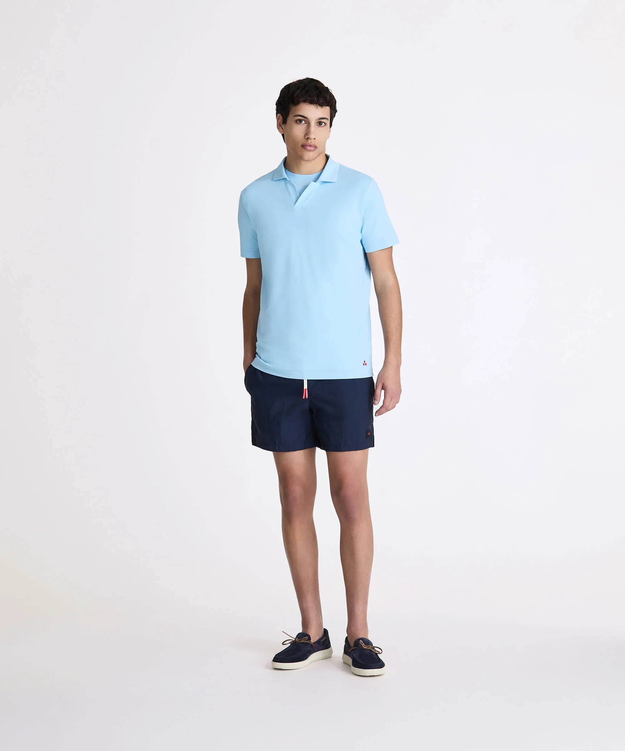 Modello uomo con polo azzurra, pantaloncini blu e mocassini in stile casual estivo.