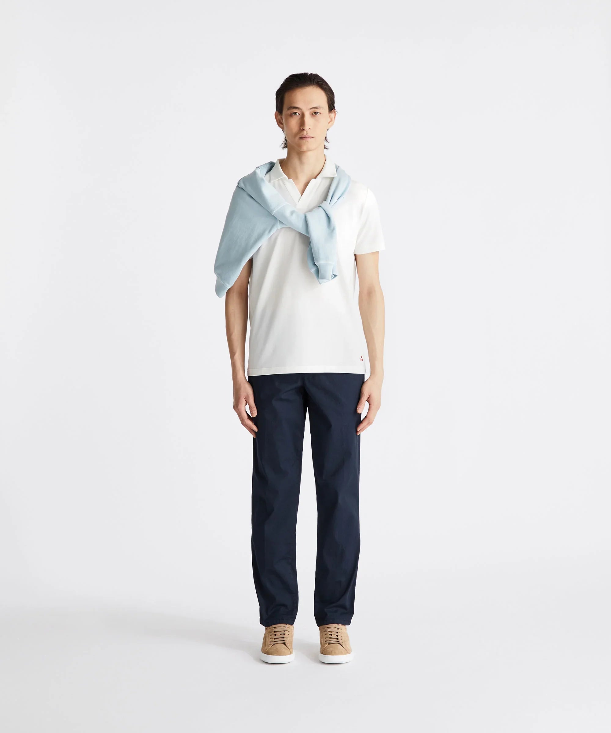 Uomo con polo bianca, pantaloni blu, maglioncino azzurro sulle spalle e sneakers beige