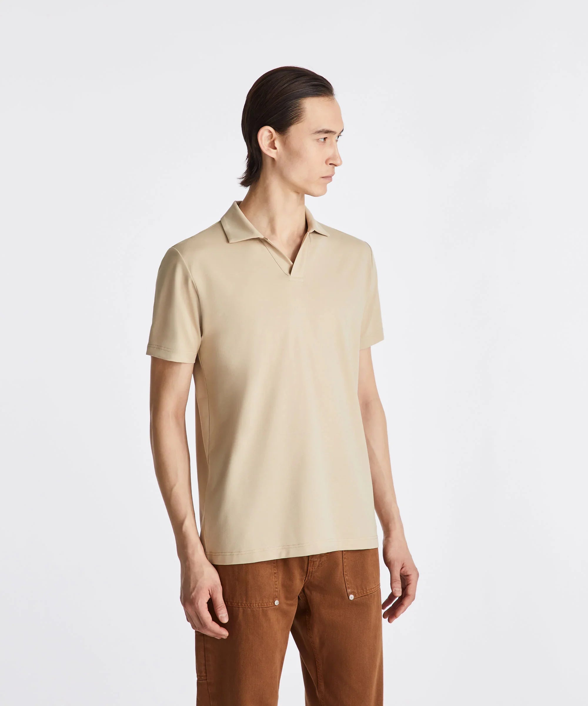 Uomo con polo beige a maniche corte e pantaloni marroni, sfondo bianco minimalista
