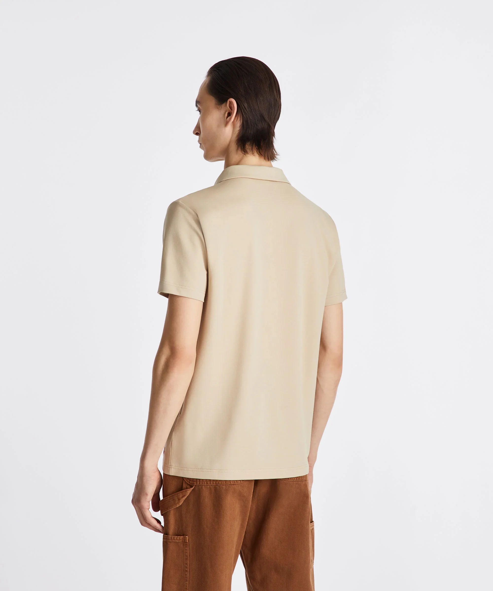 Uomo di spalle con polo beige a maniche corte e pantaloni marroni, stile casual.