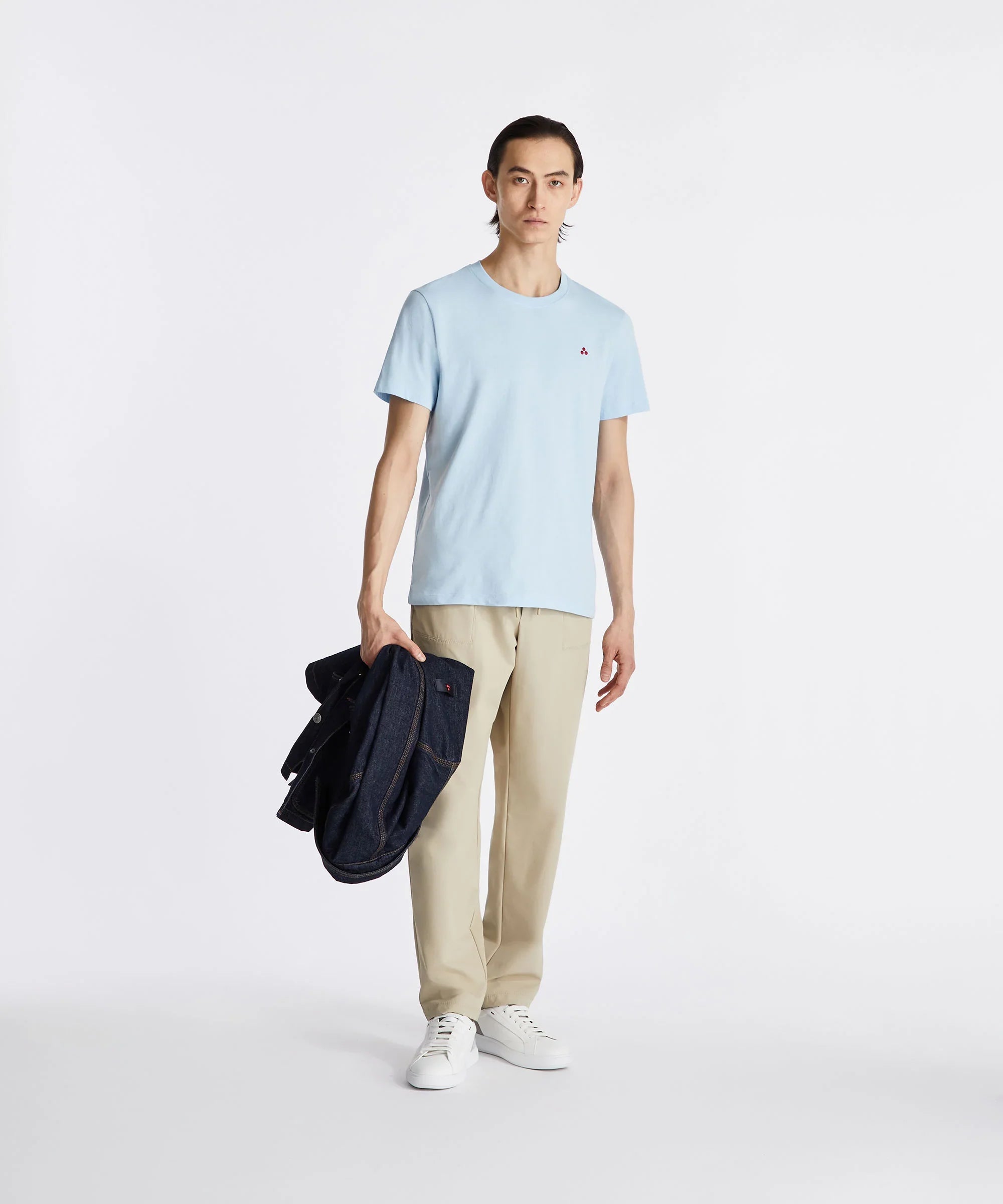 Modello indossa t-shirt azzurra, pantaloni beige e sneakers bianche, look casual uomo