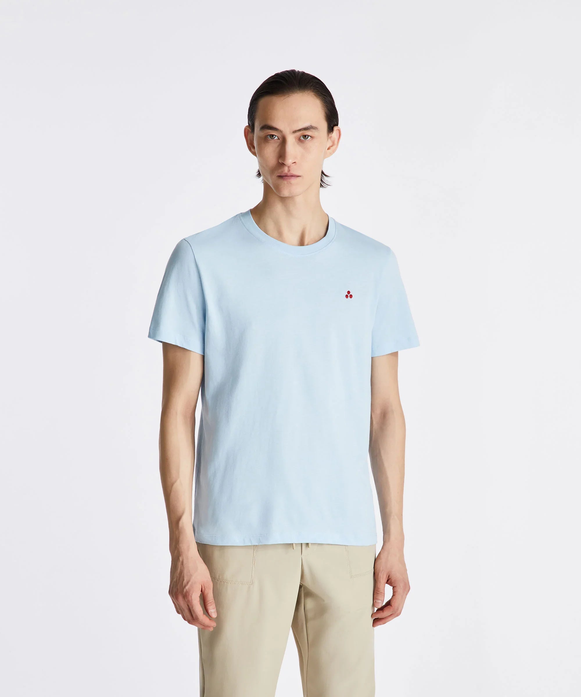 Modello uomo indossa t-shirt celeste con logo rosso, pantaloni beige, sfondo neutro.