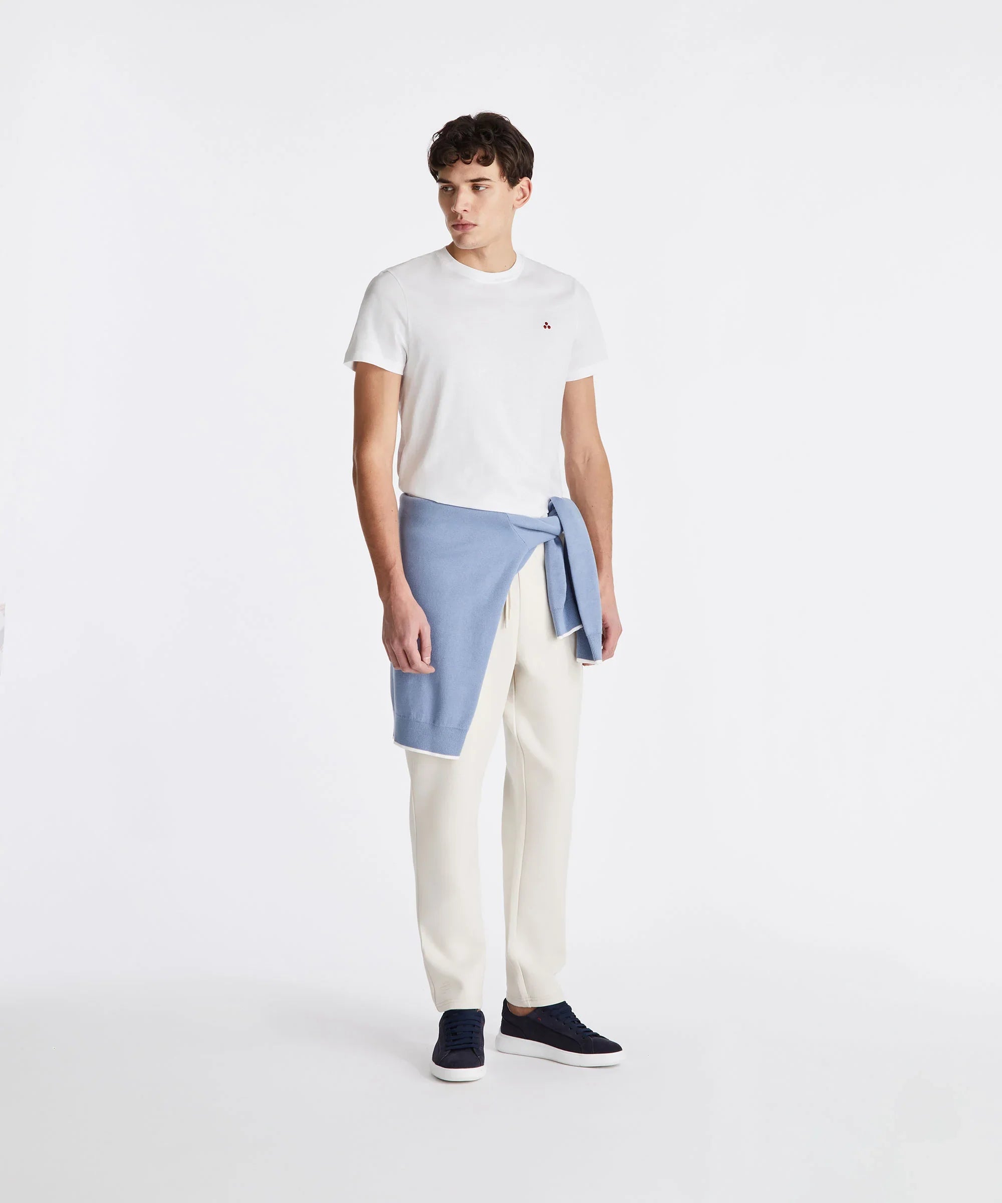 Modello indossa t-shirt bianca, pantaloni crema, maglia azzurra in vita e sneakers blu