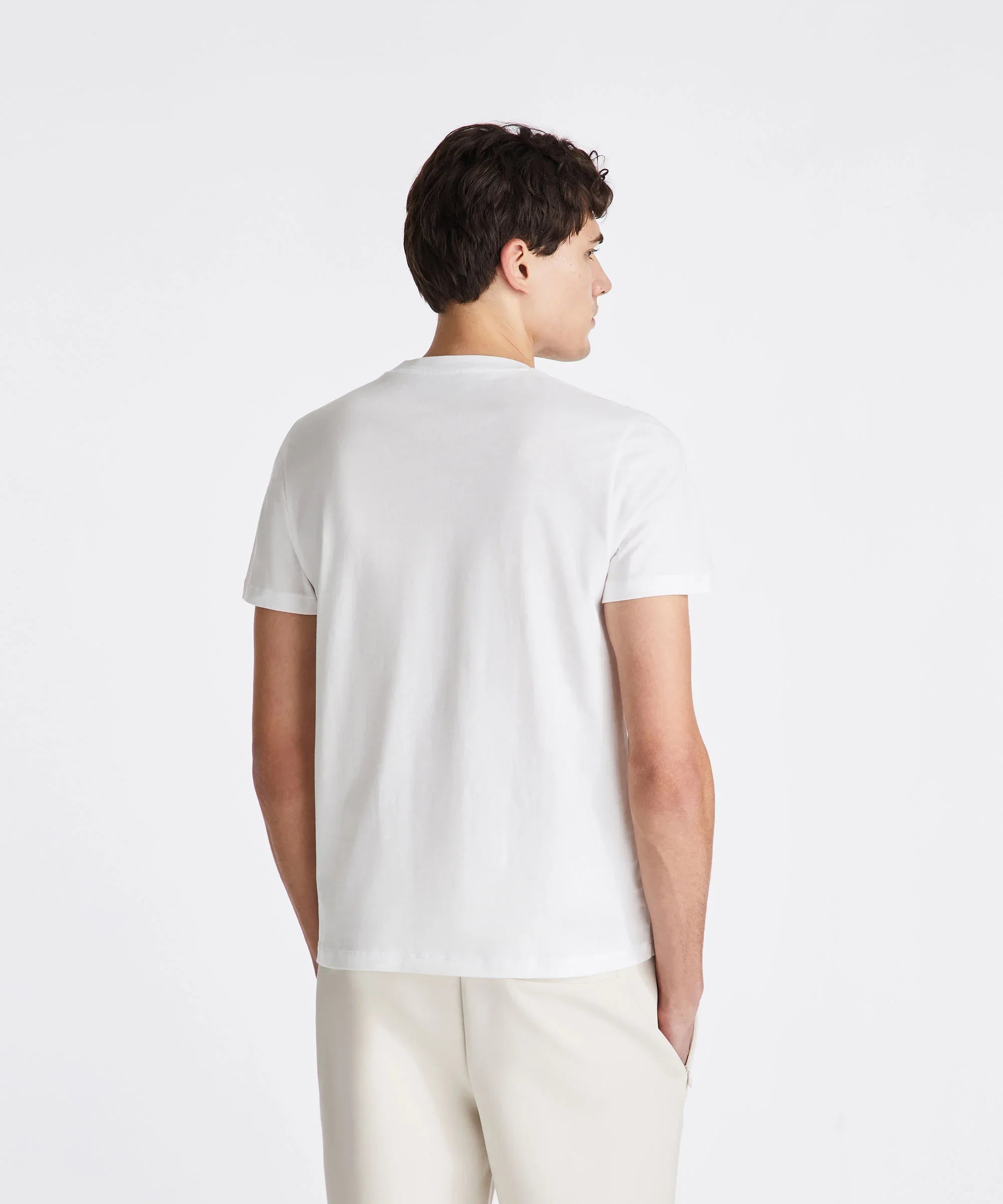 Uomo di profilo indossa t-shirt bianca e pantaloni chiari su sfondo neutro