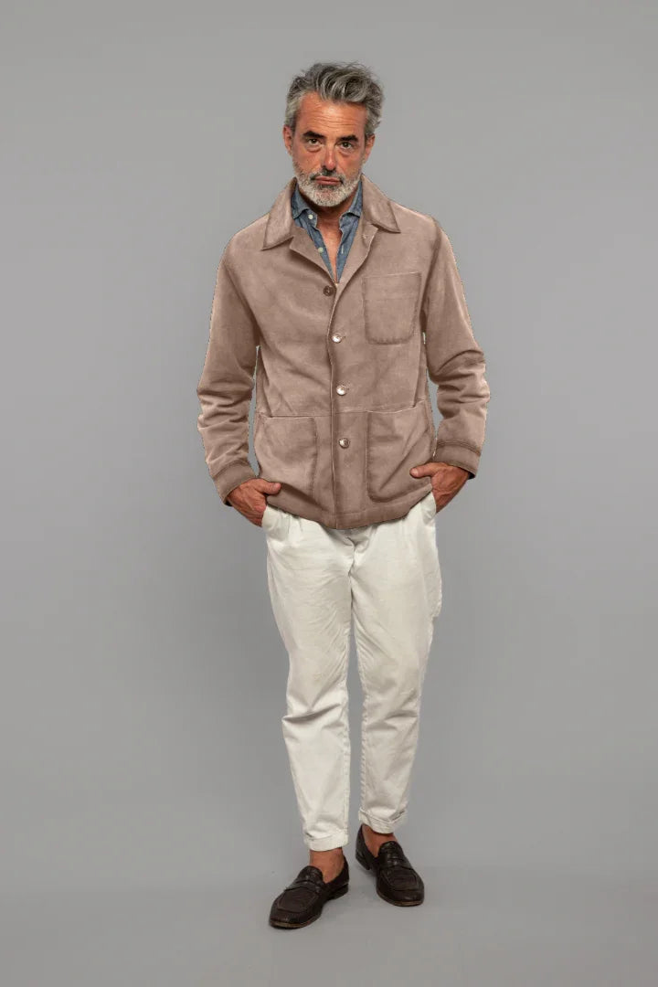 Uomo maturo con giacca beige scamosciata, camicia denim e pantaloni bianchi elegante.