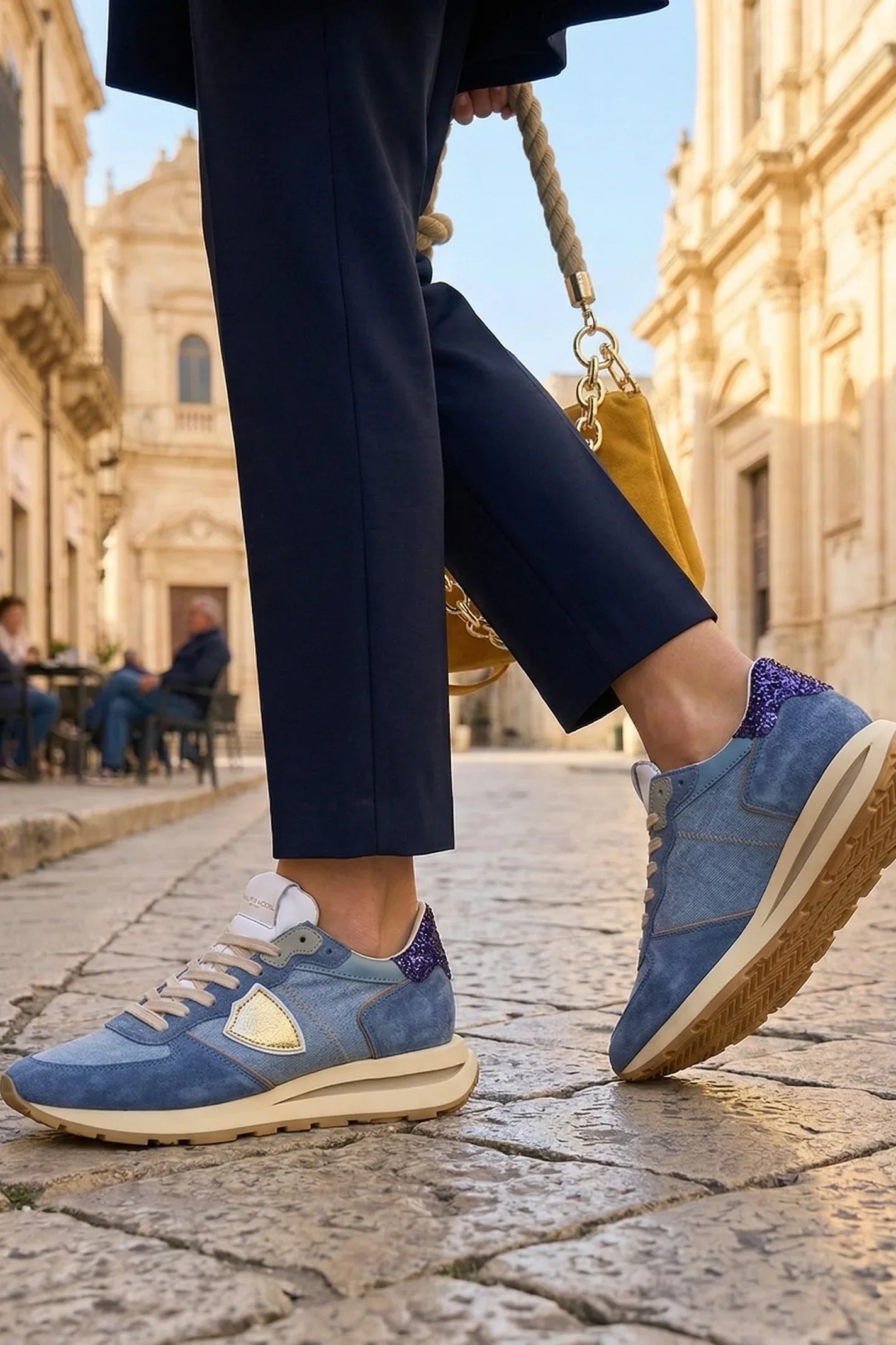 Sneakers donna in suede azzurro con dettagli glitter e pantaloni blu su strada di città storica