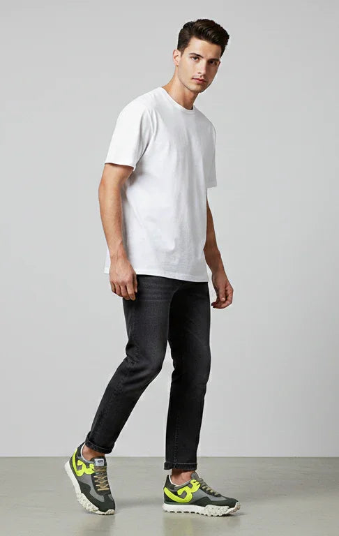 Modello uomo con t-shirt bianca, jeans neri slim e sneakers verdi gialle, look casual.