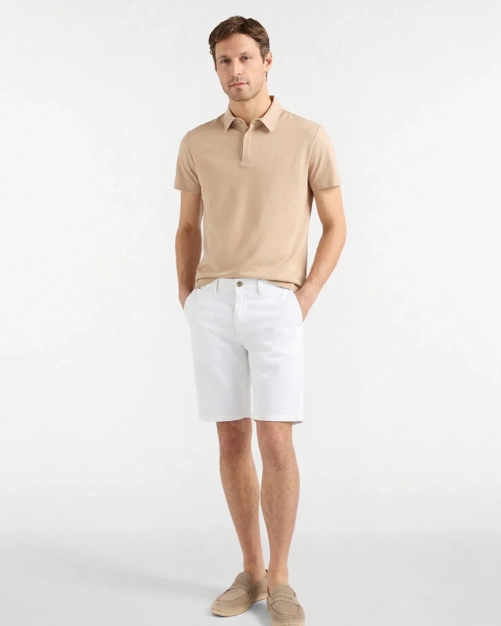 Modello uomo indossa polo beige, bermuda bianchi e mocassini beige su sfondo neutro.