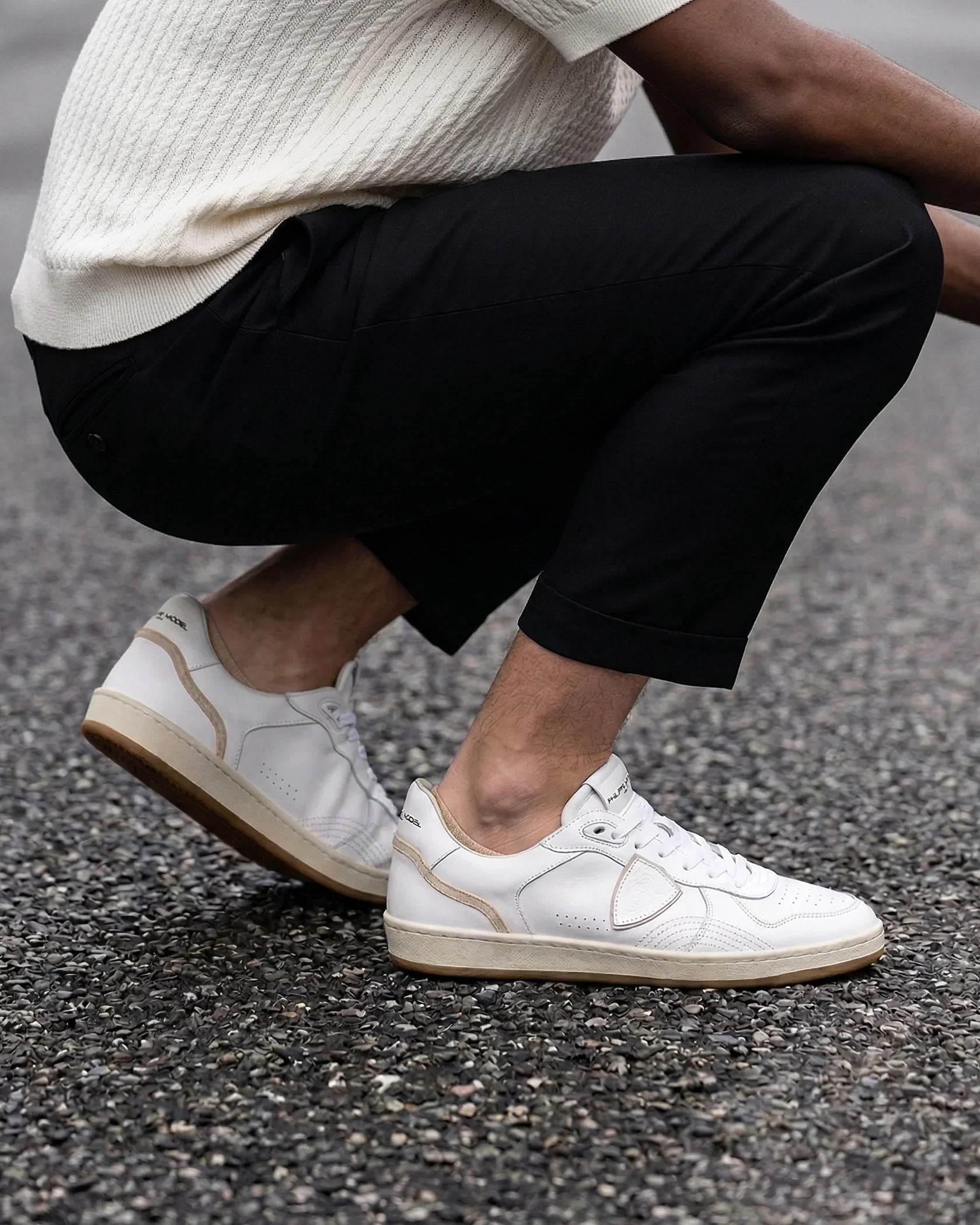 Sneakers uomo bianche in pelle con dettagli beige, indossate con pantaloni neri e maglia chiara