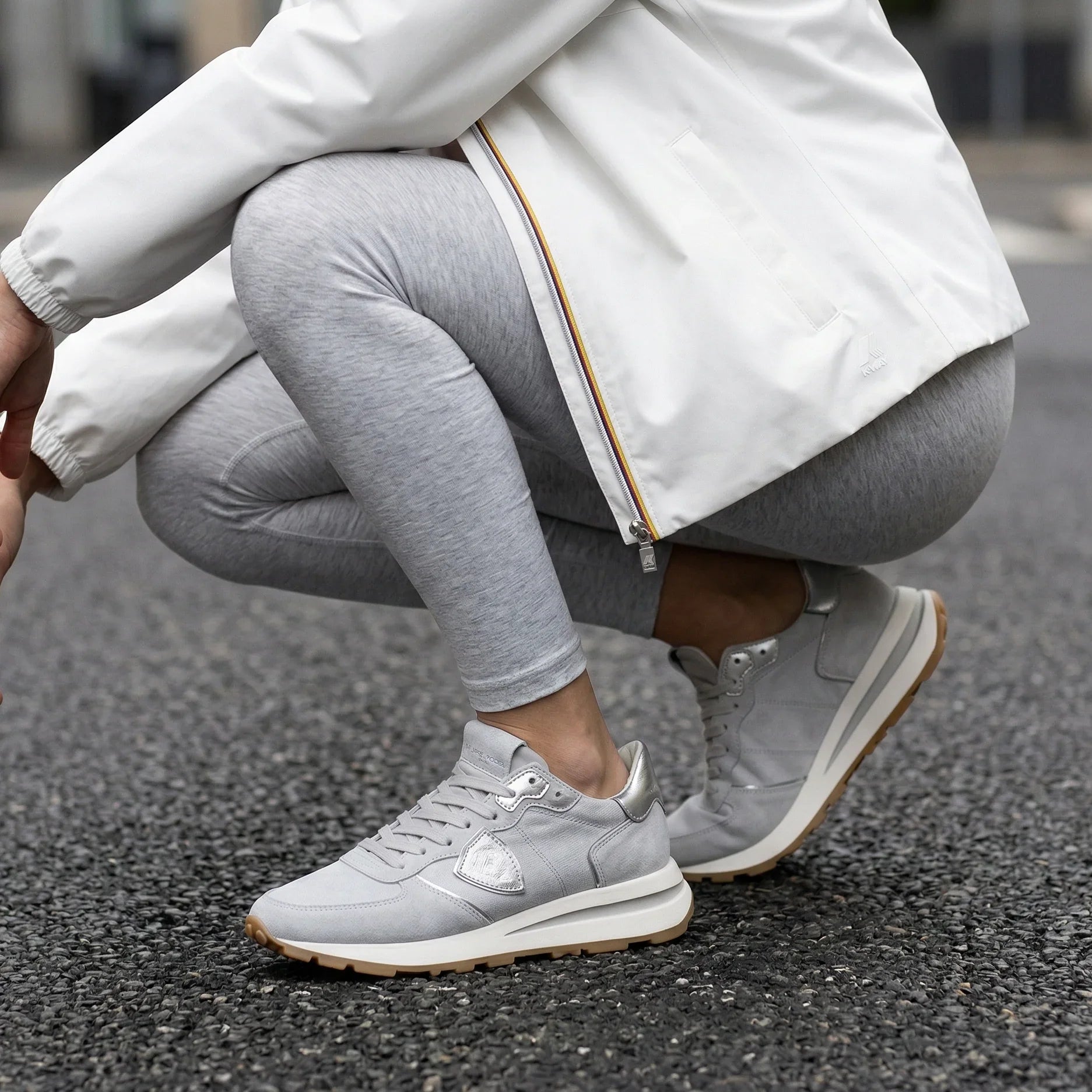 Sneakers grigie da donna abbinate a leggings chiari e giacca bianca, stile casual urbano.